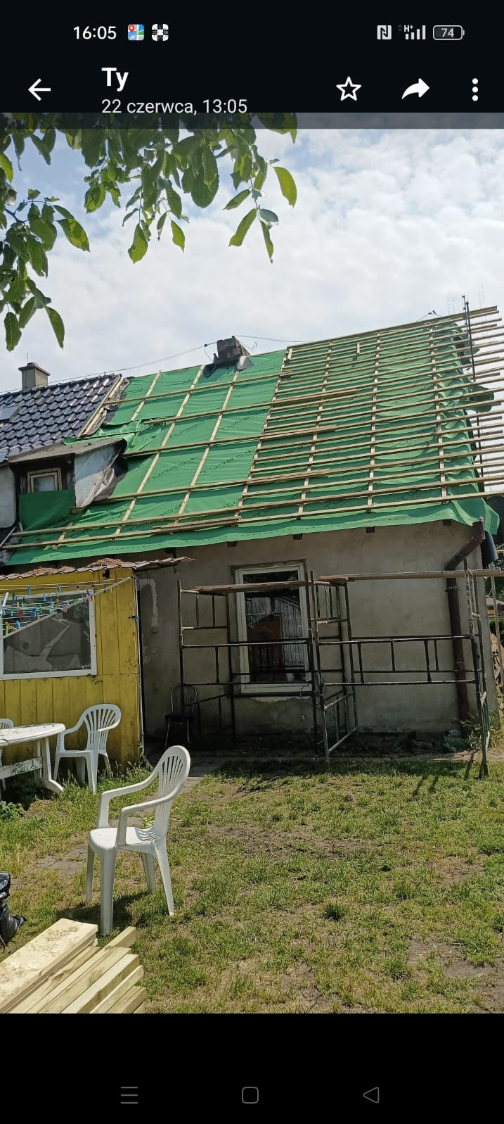 Remont dachu domu jednorodzinnego w trakcie realizacji. Widoczne rusztowania, zielona membrana i drewniane łaty. Część dachu pokryta starą dachówką.