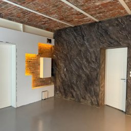 V&MHomePL VOLODYMYR MAIDAN - Loftowe wnętrze po remoncie: ceglany sufit, ściana z efektem kamienia, białe drzwi i oświetlenie LED wnęk. Nowoczesny design z surowymi elementami.