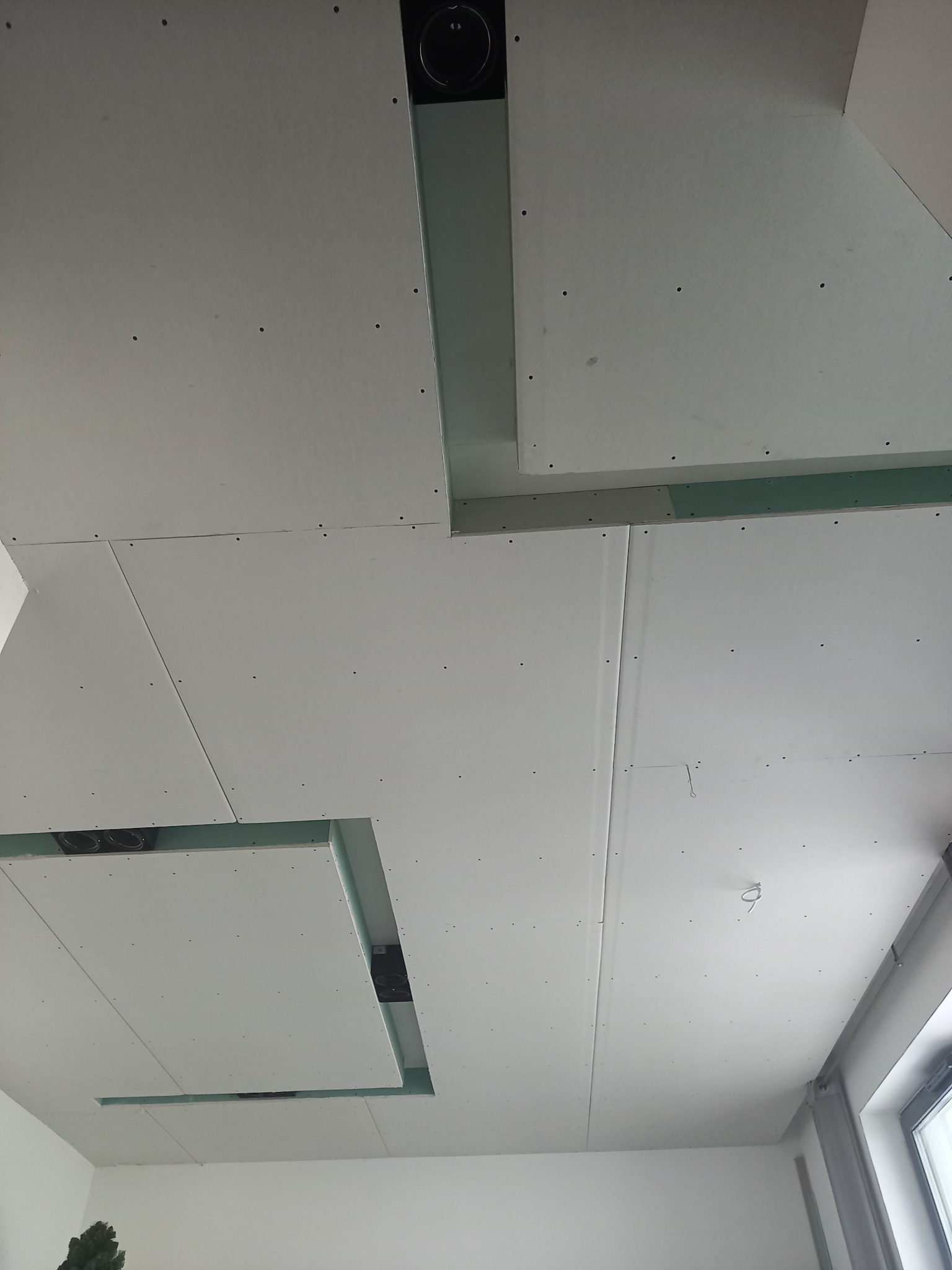 Sufit z płyt kartonowo-gipsowych z widocznymi otworami na oświetlenie i wentylację, surowy stan przed wykończeniem, widok z dołu.