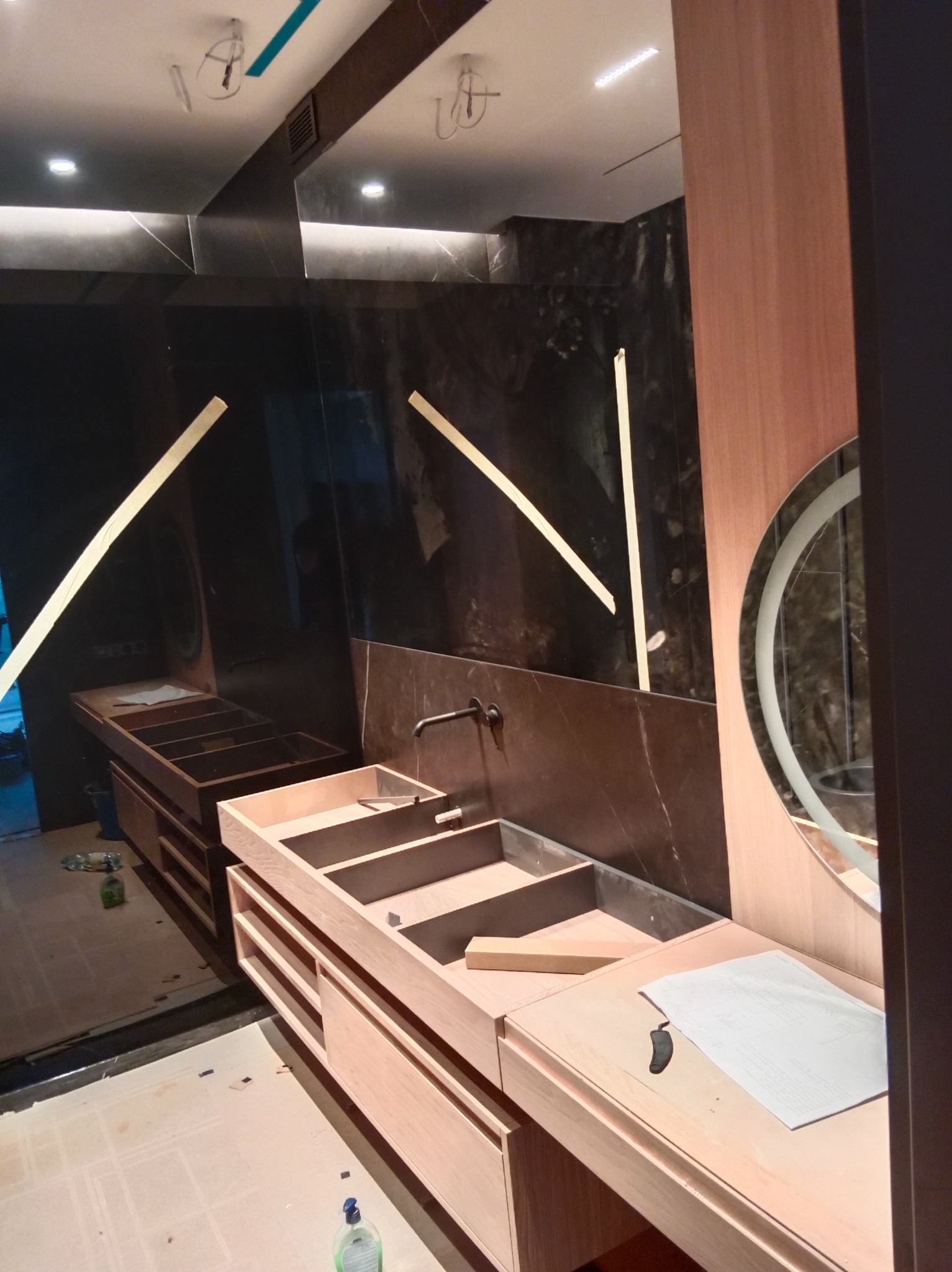 Montaż drewnianej zabudowy umywalkowej z czarną armaturą na tle marmurowej ściany z podświetleniem. Widoczne elementy instalacji i planu.