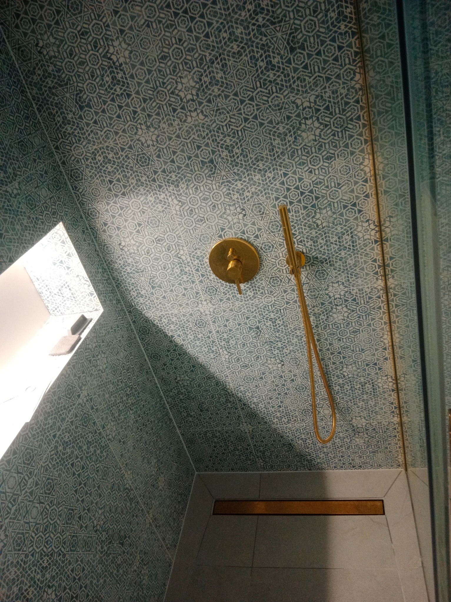 Wykończona łazienka z kabiną prysznicową, złota armatura i wzorzyste, turkusowe płytki na ścianach i suficie. Widok z dołu, podkreślający unikalny design.
