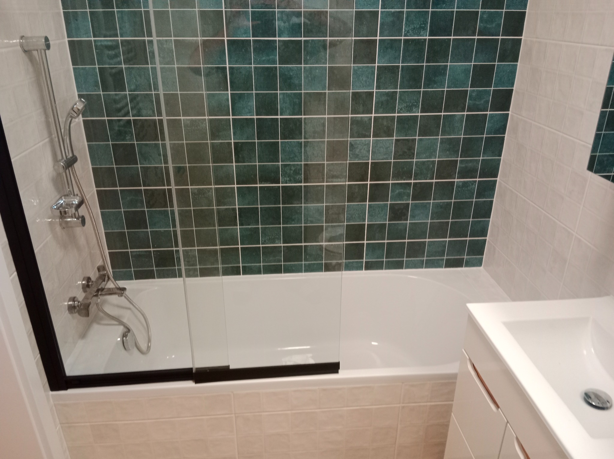 Wykończona łazienka z wanną i kabiną prysznicową, zielona mozaika na ścianie, biała umywalka z szafką. Nowoczesny design, jasne płytki podłogowe.