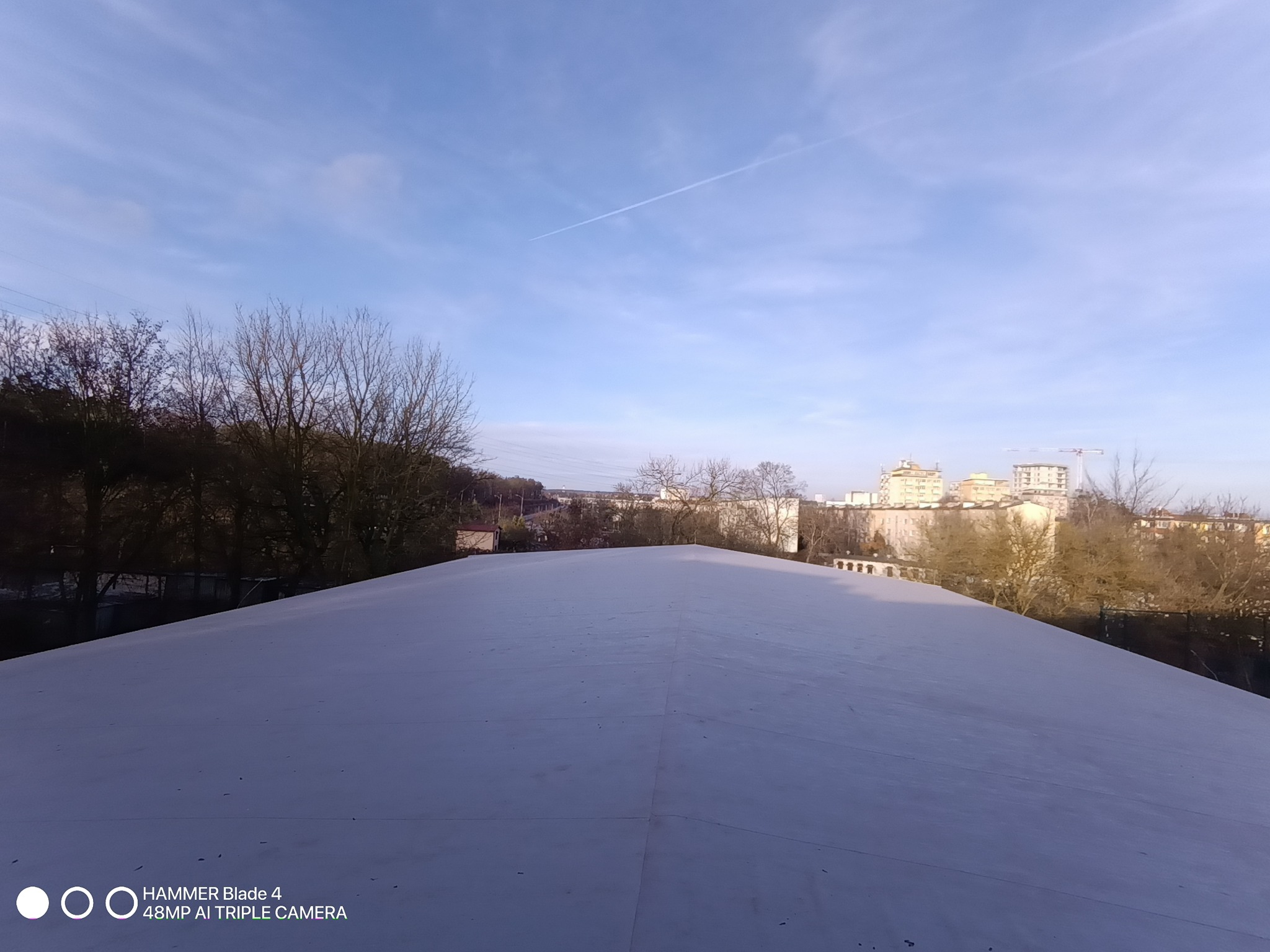 Jasny, płaski dach hali PUM w Szczecinie, widziany z góry w słoneczny dzień. W tle zabudowa miejska i błękitne niebo z delikatną smugą kondensacyjną.