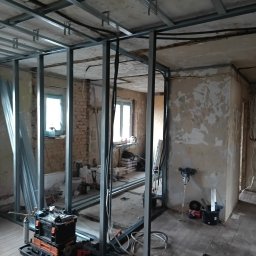 Sylwester Bieniecki - Montaż metalowej konstrukcji ścianki działowej z płyt gipsowo-kartonowych w remontowanym pomieszczeniu. Widoczne narzędzia i materiały budowlane.