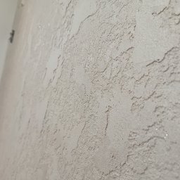 Sylwester Bieniecki - Teksturowana ściana w odcieniach beżu, z widoczną fakturą i delikatnym połyskiem, sfotografowana pod kątem, ukazująca detale wykończenia.