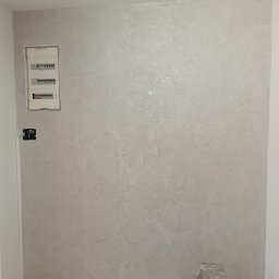 Sylwester Bieniecki - Dekoracyjna ściana po szpachlowaniu w Kłodzku z widoczną fakturą, zabezpieczona podłoga i drabina. Wykończenie wnętrza z detalami elektrycznymi.