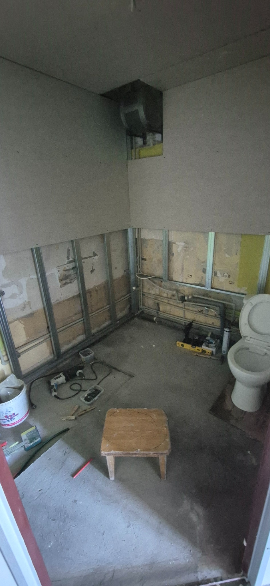 Łazienka w trakcie remontu: widoczne stelaże, częściowo położona płyta karton-gips, instalacje i narzędzia. Ujęcie z góry, na pierwszym planie drewniany taboret.