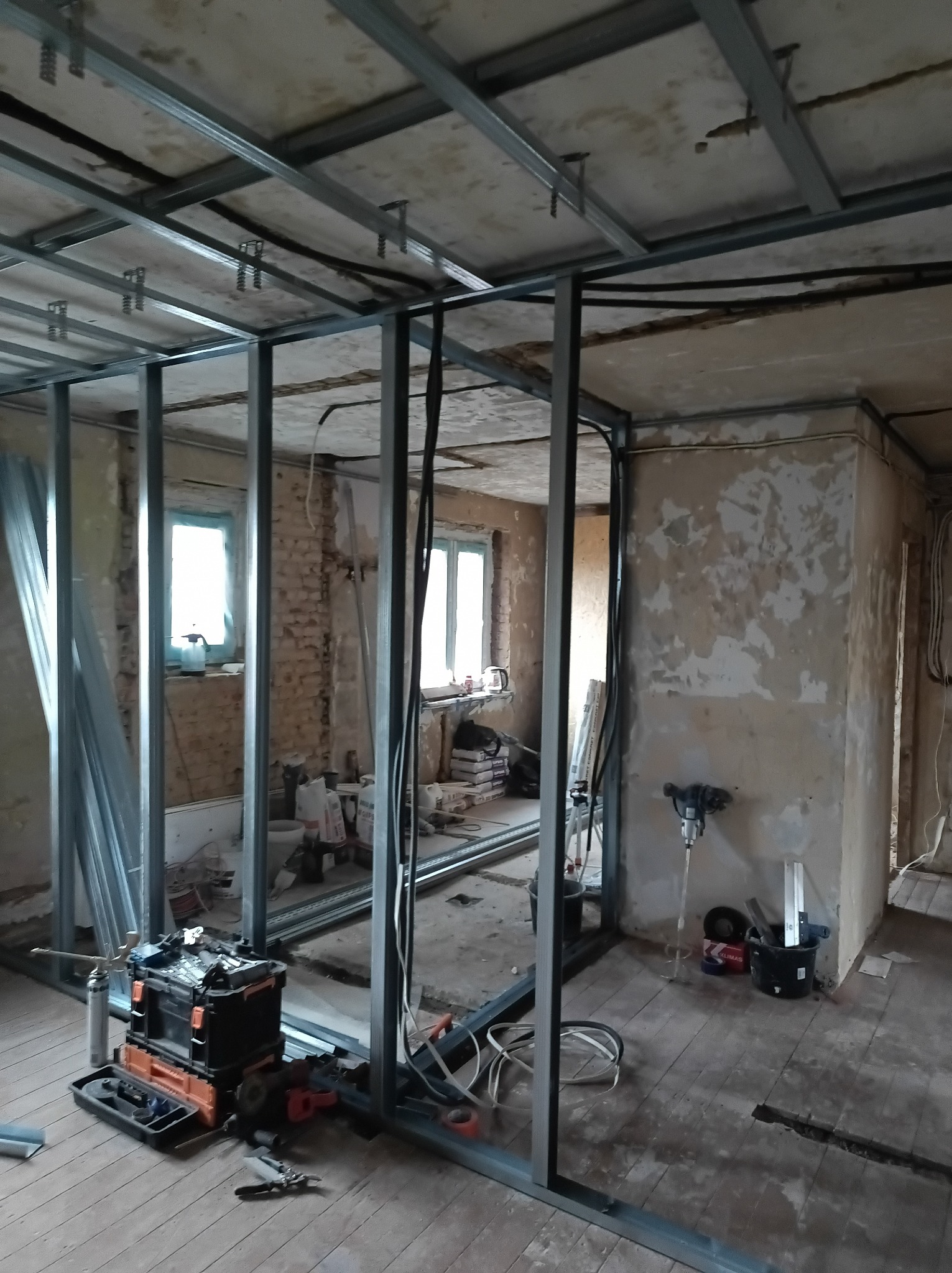 Montaż metalowej konstrukcji ścianki działowej z płyt gipsowo-kartonowych w remontowanym pomieszczeniu. Widoczne narzędzia i materiały budowlane.