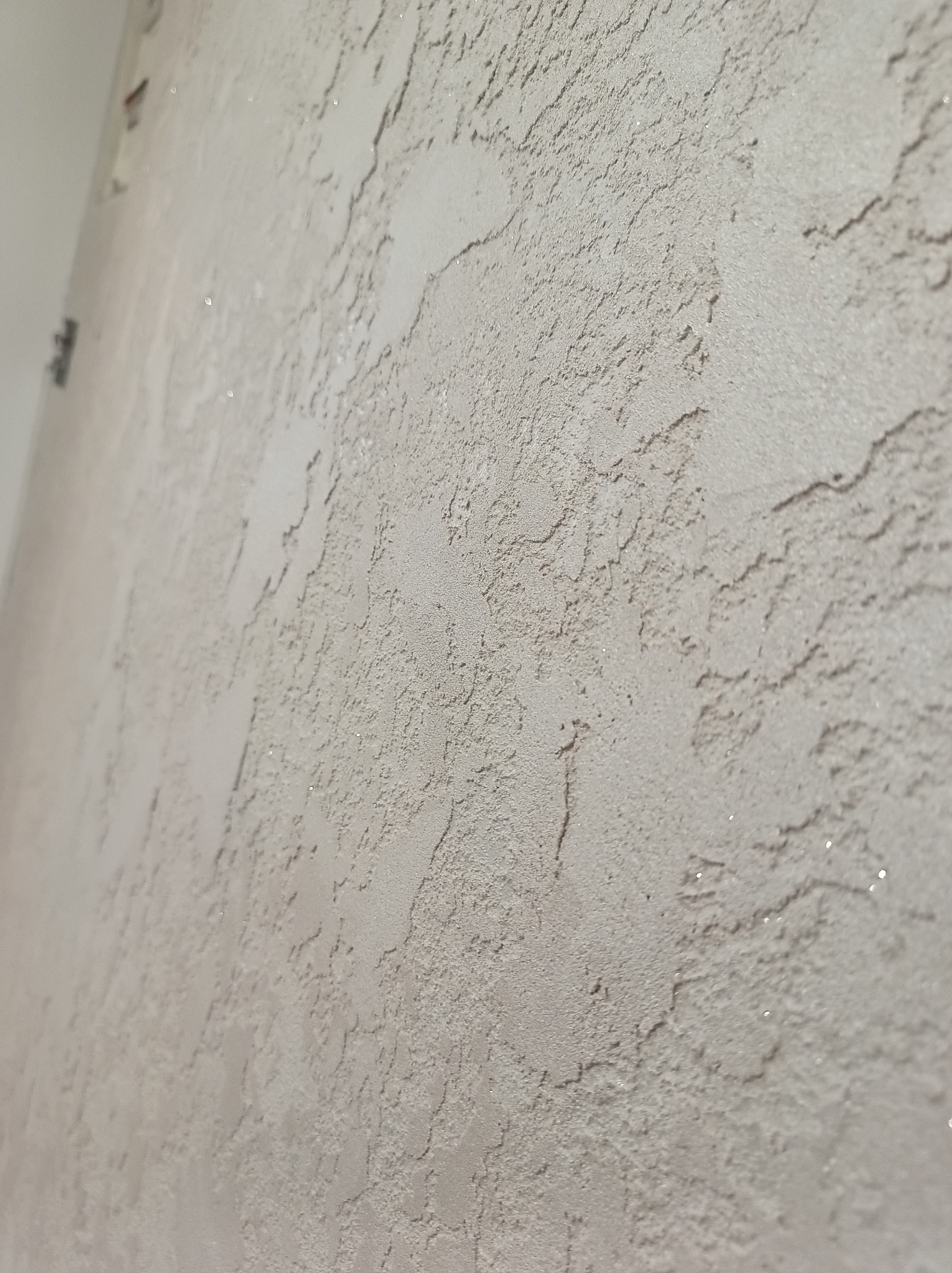 Teksturowana ściana w odcieniach beżu, z widoczną fakturą i delikatnym połyskiem, sfotografowana pod kątem, ukazująca detale wykończenia.