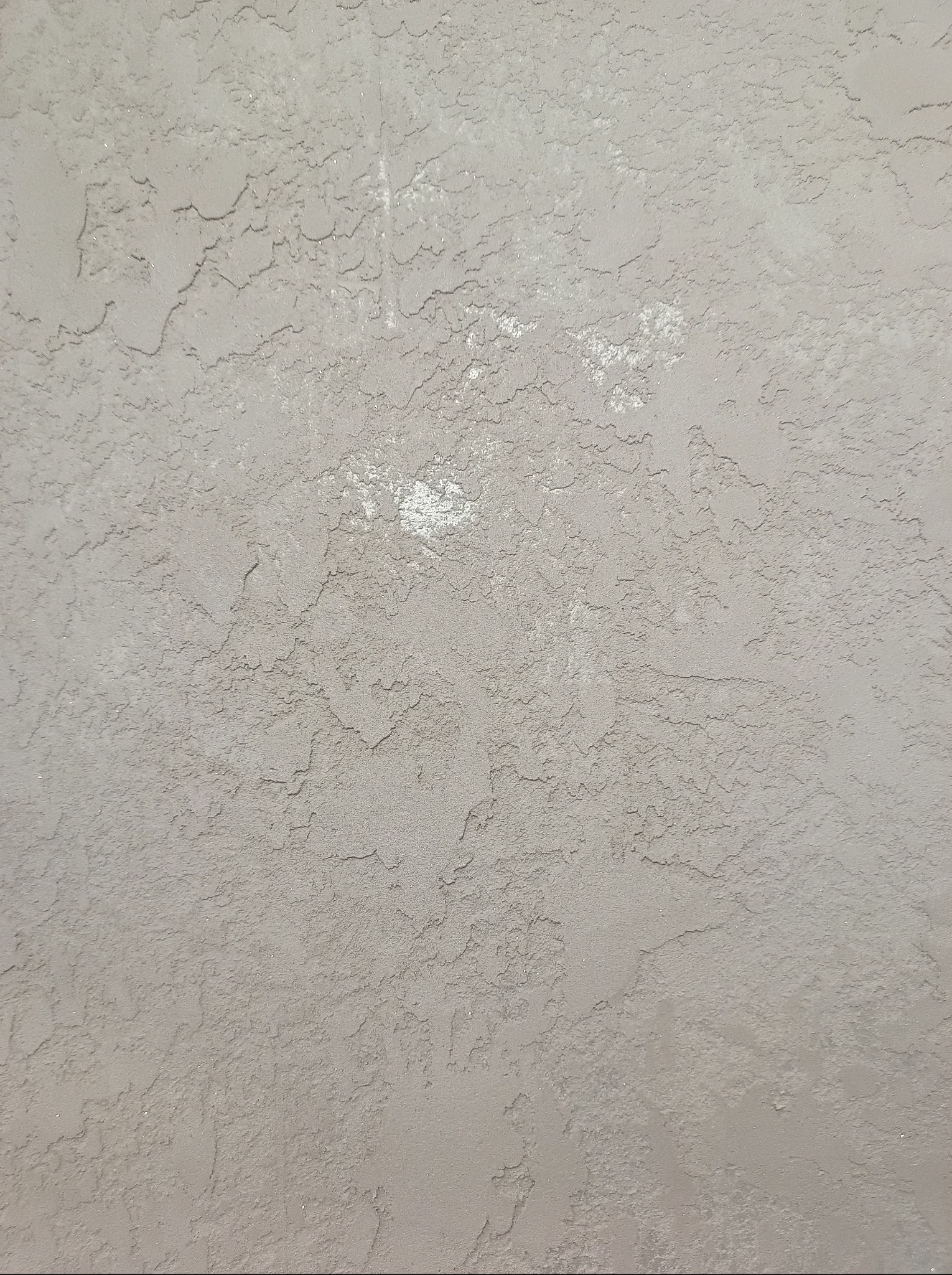 Szara ściana z wyraźną, nieregularną fakturą. Widoczne drobne nierówności i delikatne cieniowanie, tworzące efekt trójwymiarowości. Neutralna kolorystyka.