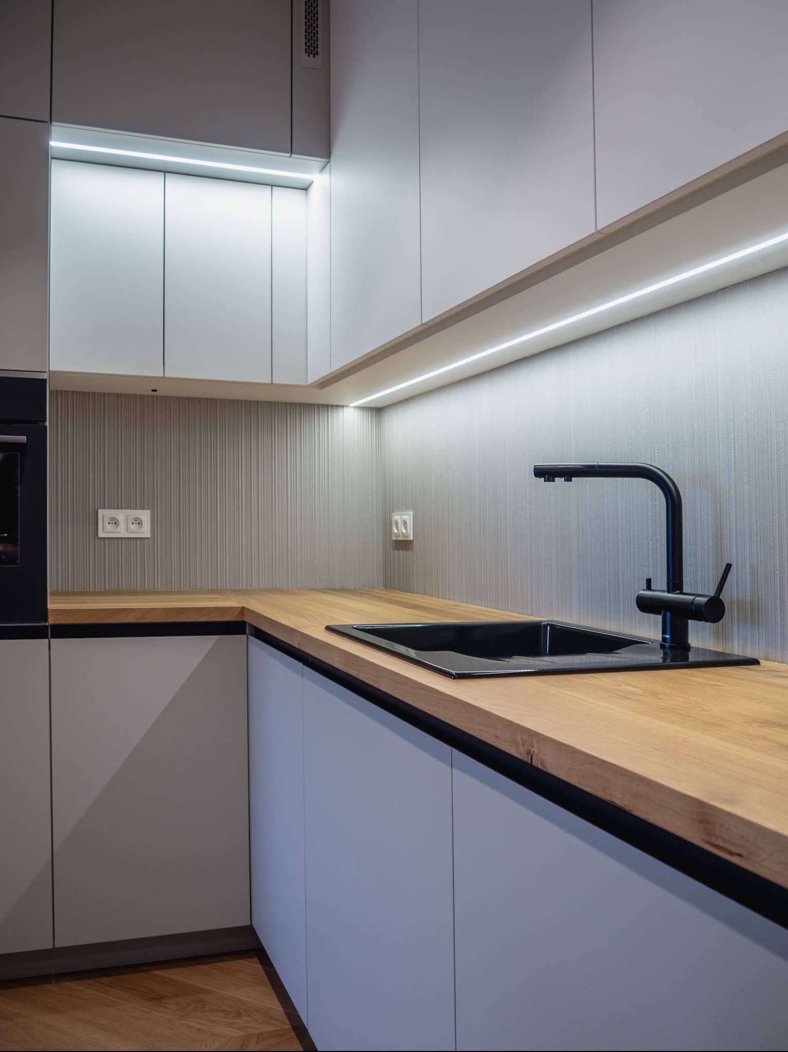 Nowoczesna kuchnia w Kłodzku: drewniany blat, czarny zlew i bateria, szare szafki z oświetleniem LED. Minimalistyczny design i funkcjonalność.