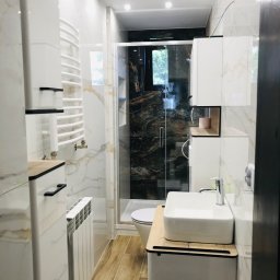 DAR-HAUS DARIUSZ NOWAK USŁUGI OGÓLNOBUDOWLANE - Nowoczesna łazienka z kabiną prysznicową typu walk-in, białą armaturą i grzejnikiem drabinkowym. Marmurowe płytki na ścianach i drewnopodobna podłoga.