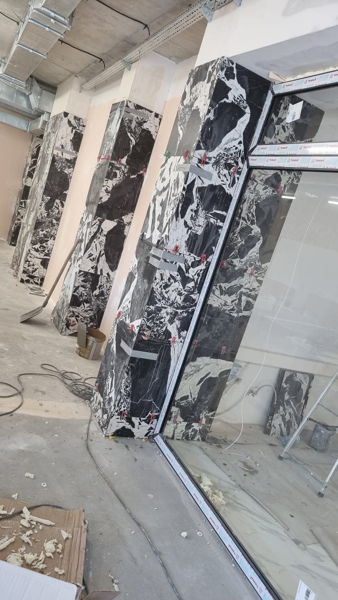 Montaż czarnych płyt imitujących marmur na ścianach, widoczne narzędzia i elementy montażowe. Prace wykończeniowe w surowym wnętrzu.