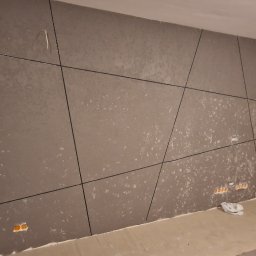 DB ElektroSystem - Panel dekoracyjny na ścianie z widocznymi gniazdkami elektrycznymi. Geometryczny wzór paneli w odcieniach szarości. Widoczne przygotowania do montażu.