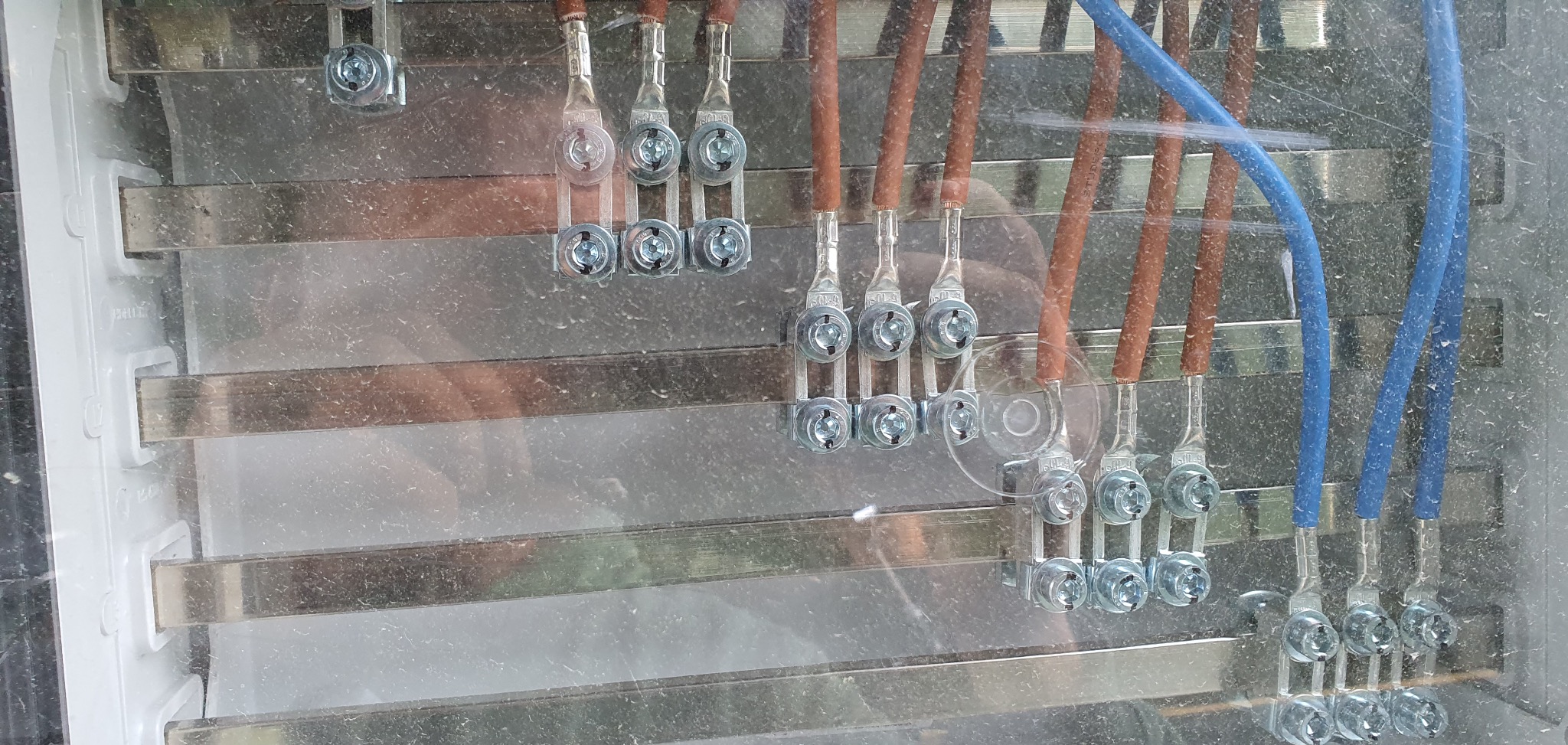 Szczegółowe ujęcie podłączenia przewodów elektrycznych (brązowych i niebieskich) do listwy zaciskowej w skrzynce rozdzielczej. Widoczne metalowe elementy mocujące.