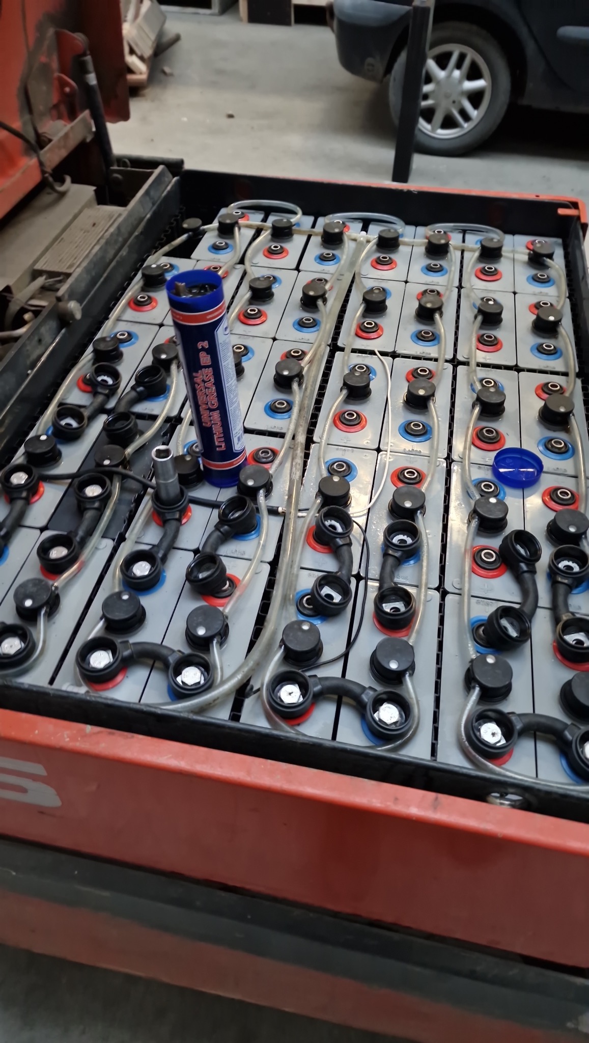 Bateria trakcyjna w wózku widłowym, z widocznym smarem litowym i narzędziem. Układ ogniw z przewodami i złączkami. Konserwacja lub naprawa baterii.