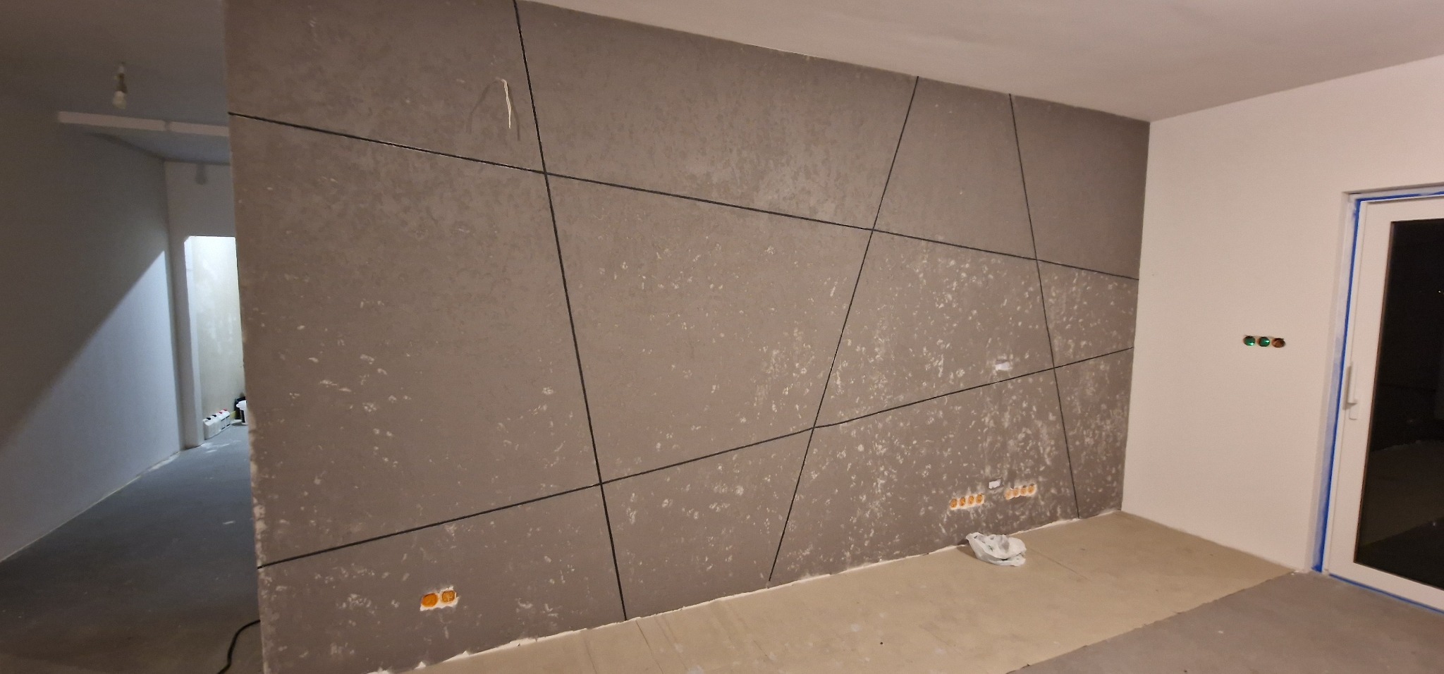 Panel dekoracyjny na ścianie z widocznymi gniazdkami elektrycznymi. Geometryczny wzór paneli w odcieniach szarości. Widoczne przygotowania do montażu.