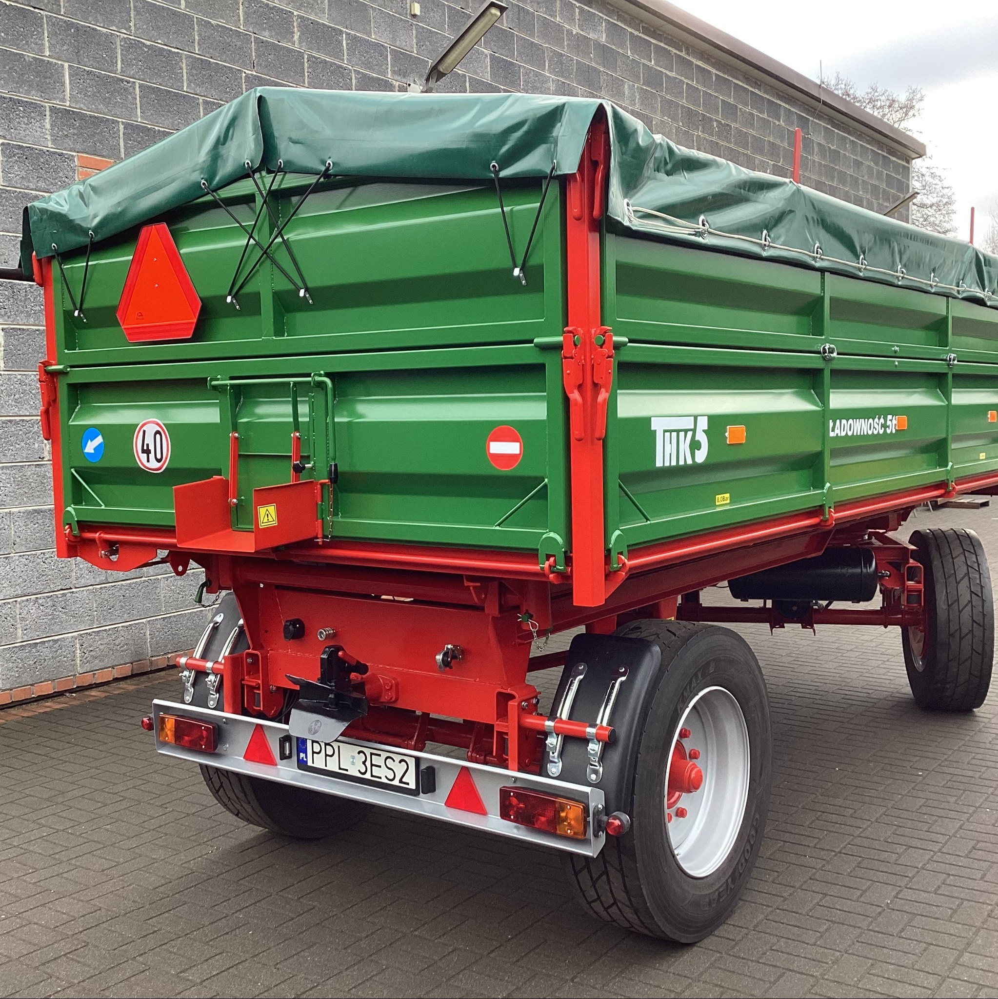 Zielono-czerwona przyczepa rolnicza THK5 z plandeką, widok z tyłu, tablica rejestracyjna PPL 3ES2, opony, światła. Solidna konstrukcja na tle szarej ściany.