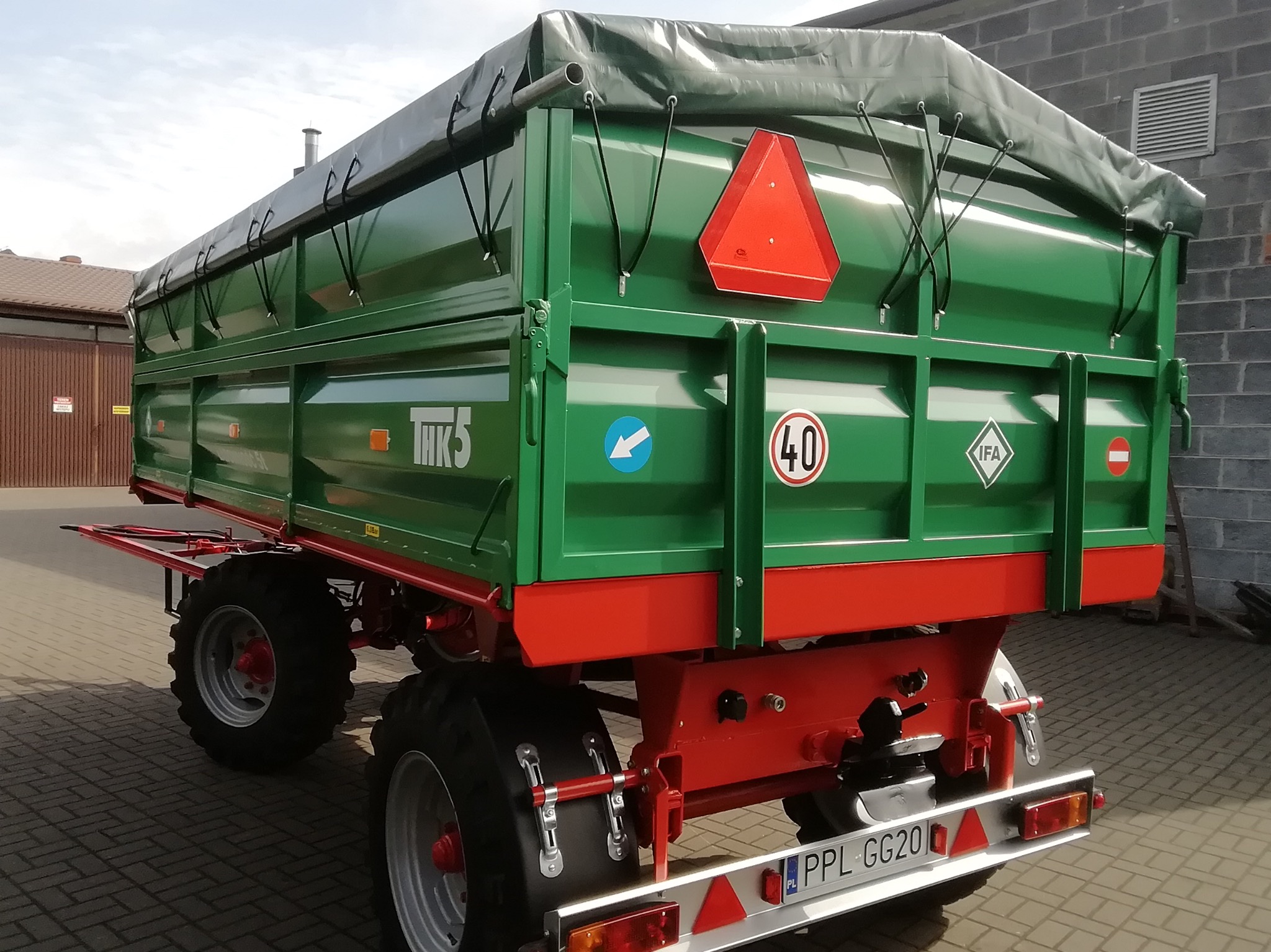 Zielona przyczepa rolnicza z plandeką, widok z tyłu, z czerwonymi elementami konstrukcyjnymi i tablicą rejestracyjną. Widoczne oznaczenia THK 5, IFA i ograniczenie prędkości 40.