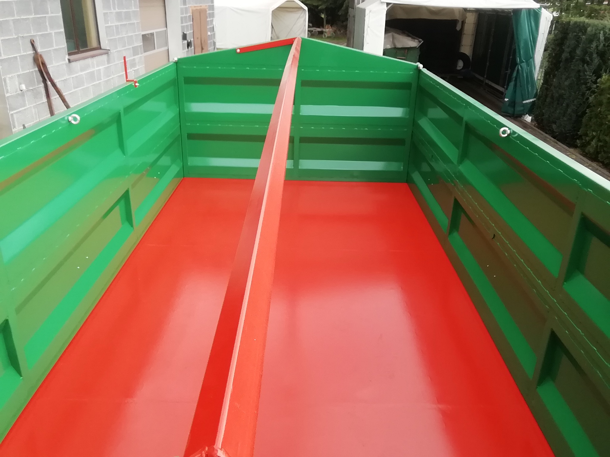 Wnętrze nowej, pomalowanej na zielono i czerwono metalowej przyczepy rolniczej z centralnym wzmocnieniem, widok z góry, świeża farba.