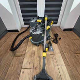 ABM Pro Łukasz Motłoch - Profesjonalny odkurzacz piorący Karcher z akcesoriami na drewnianej podłodze, gotowy do prania dywanów lub tapicerki. Widoczne okno i rolety w tle.