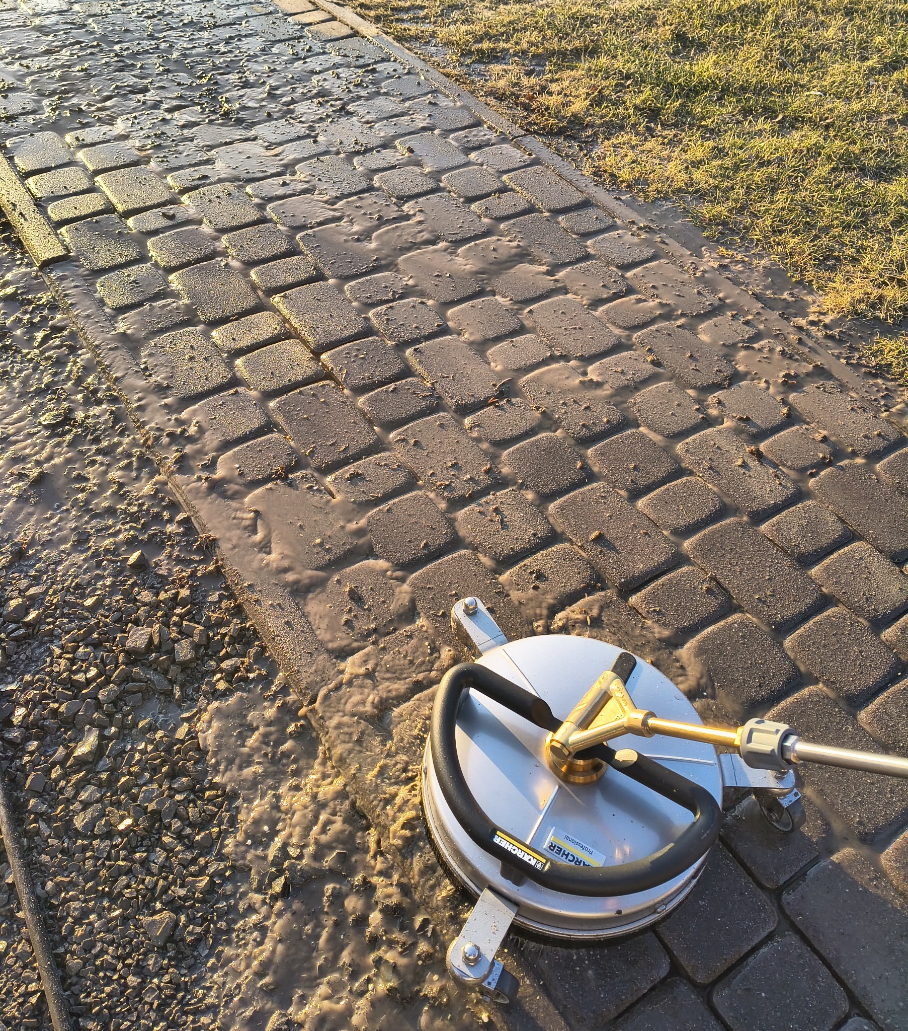 Czyszczenie kostki brukowej urządzeniem Karcher. Widoczna różnica między czystą a brudną powierzchnią. Woda i błoto na kostce. Słoneczne oświetlenie.
