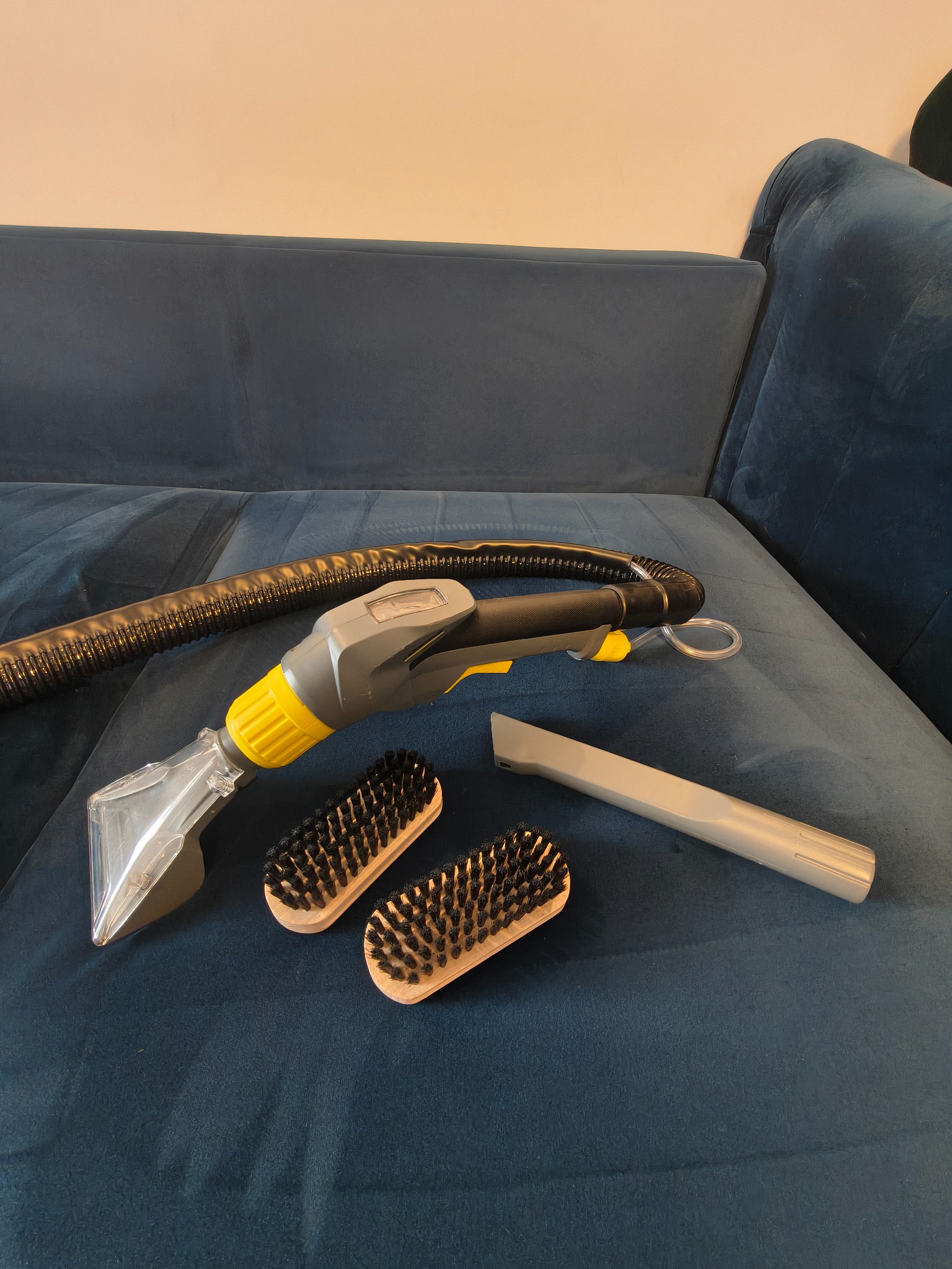 Dysza do prania tapicerki, szczotki i ssawka na granatowej kanapie. Sprzęt do czyszczenia mebli tapicerowanych w zbliżeniu, gotowy do użycia.