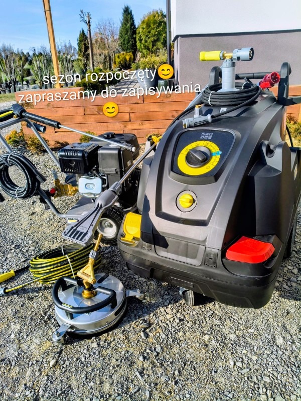 Profesjonalna myjka ciśnieniowa Karcher z akcesoriami do czyszczenia powierzchni, gotowa do użycia na zewnątrz. Widoczne detale urządzenia i otoczenie.