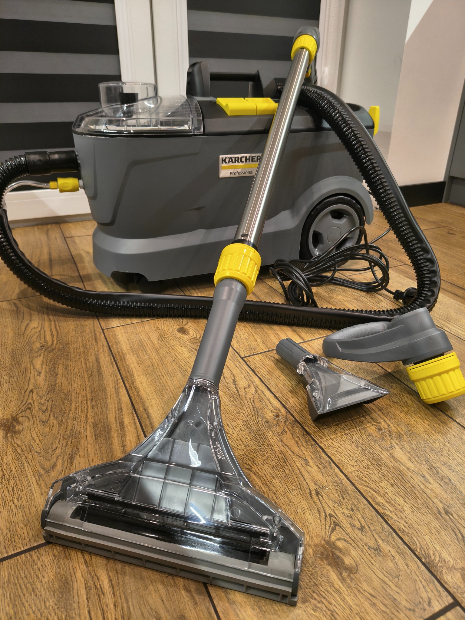 Profesjonalny odkurzacz piorący Kärcher z przezroczystą dyszą do tapicerki, wężykiem i dodatkowymi końcówkami na drewnianej podłodze. Sprzęt do czyszczenia.