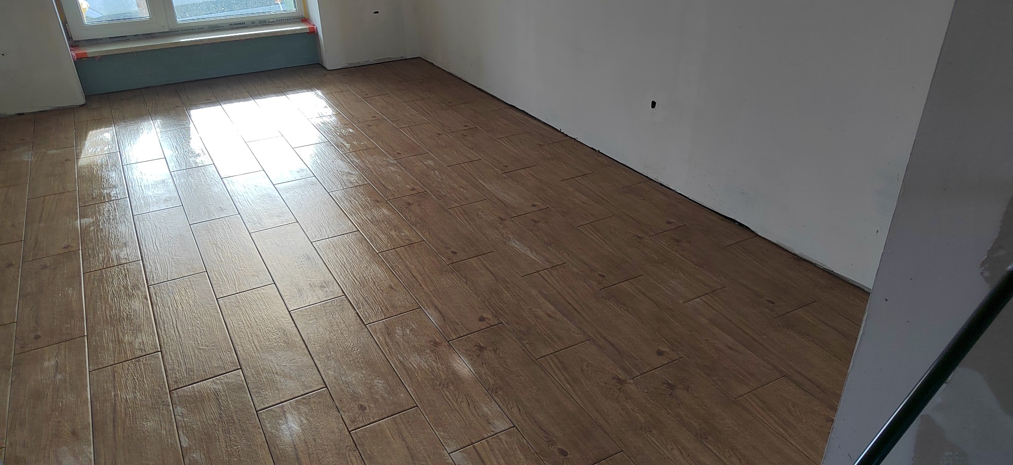 Ułożona podłoga z płytek imitujących drewno w Łoniowie, widok z góry, świeżo po umyciu, z widocznym oknem w tle i fragmentem ściany.