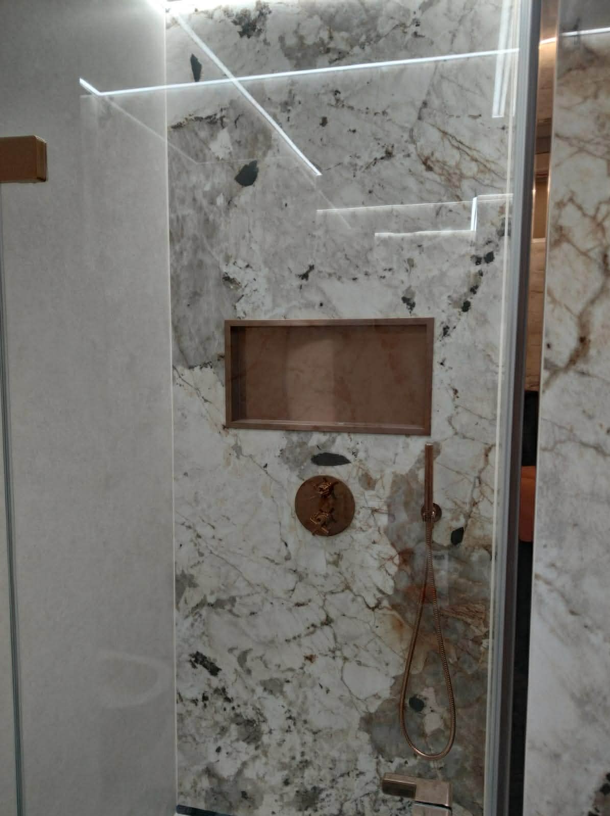 Kabina prysznicowa z marmurową ścianą, wnęką i miedzianą armaturą. Nowoczesny design z podświetleniem LED.