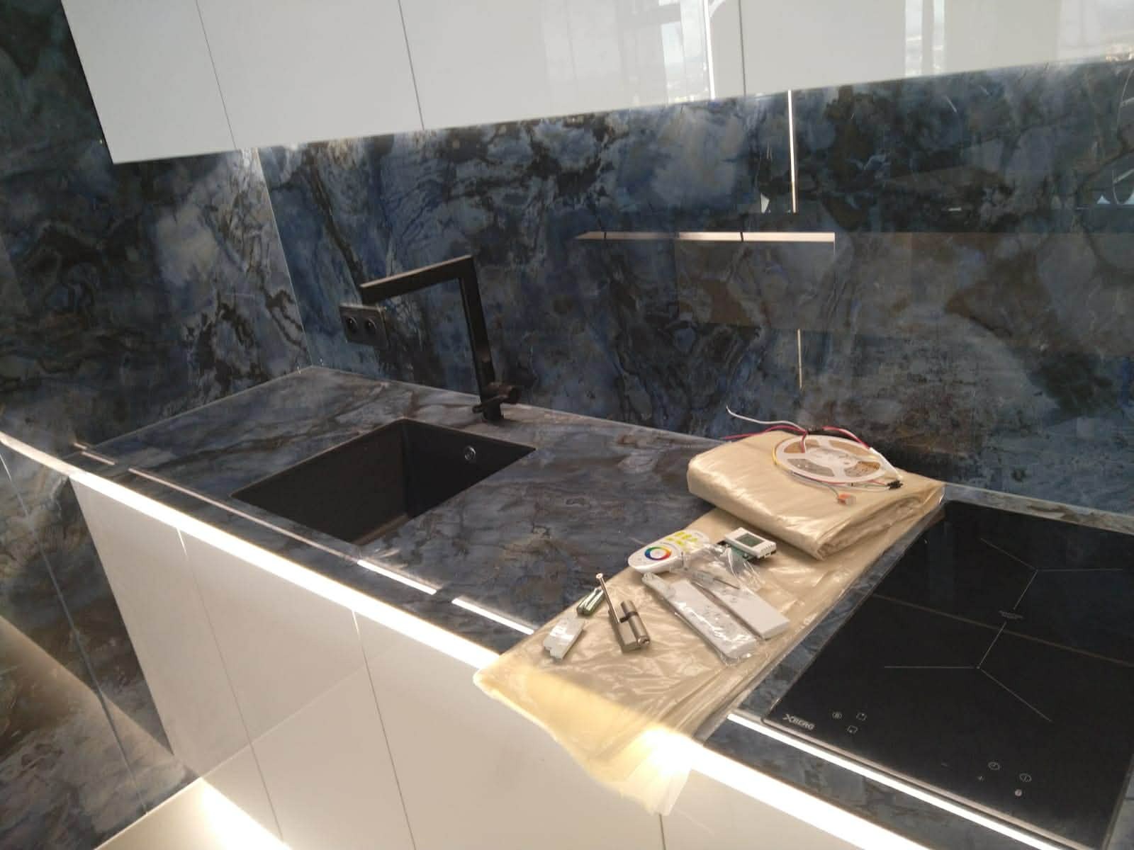 Nowoczesna kuchnia z blatem i ścianą w odcieniach granatu, czarny zlew i bateria, płyta indukcyjna. Na blacie akcesoria do montażu oświetlenia LED.