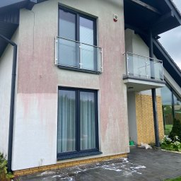 MK Błysk - Dwupiętrowy dom z elewacją w trakcie czyszczenia. Widoczne zacieki i pozostałości po myciu na jasnej fasadzie. Nowoczesna architektura z balkonami i dużymi oknami.