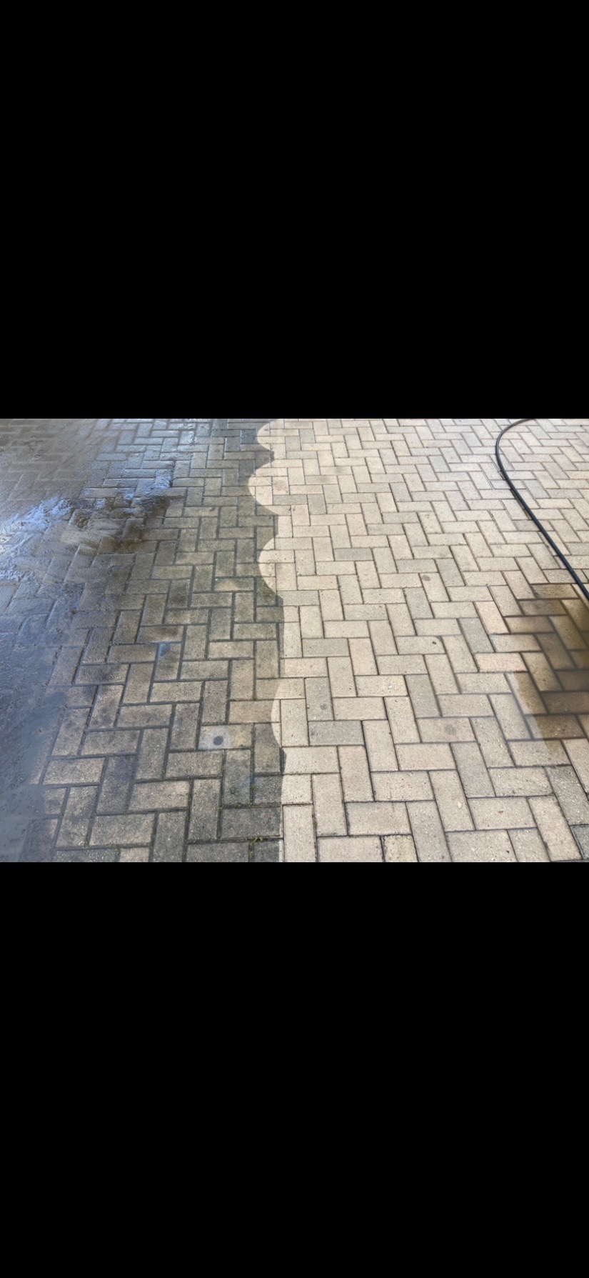 Kostka brukowa częściowo umyta, ukazująca różnicę w wyglądzie przed i po czyszczeniu. Widoczna linia podziału i fragment węża ciśnieniowego.