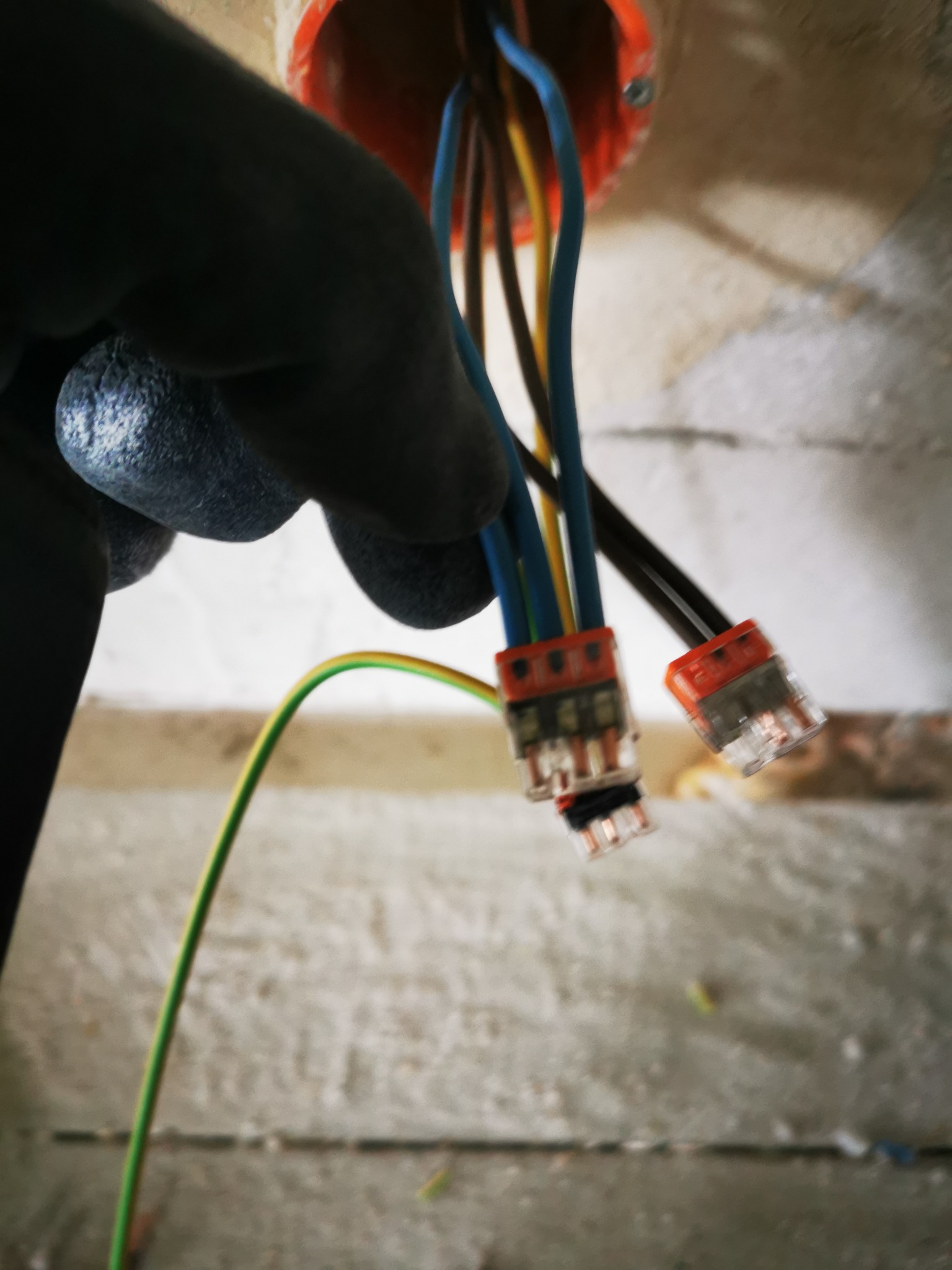 Instalacja elektryczna w puszce: przewody (niebieski, żółty, brązowy, zielono-żółty) połączone złączkami WAGO, widoczne w trakcie prac instalacyjnych.