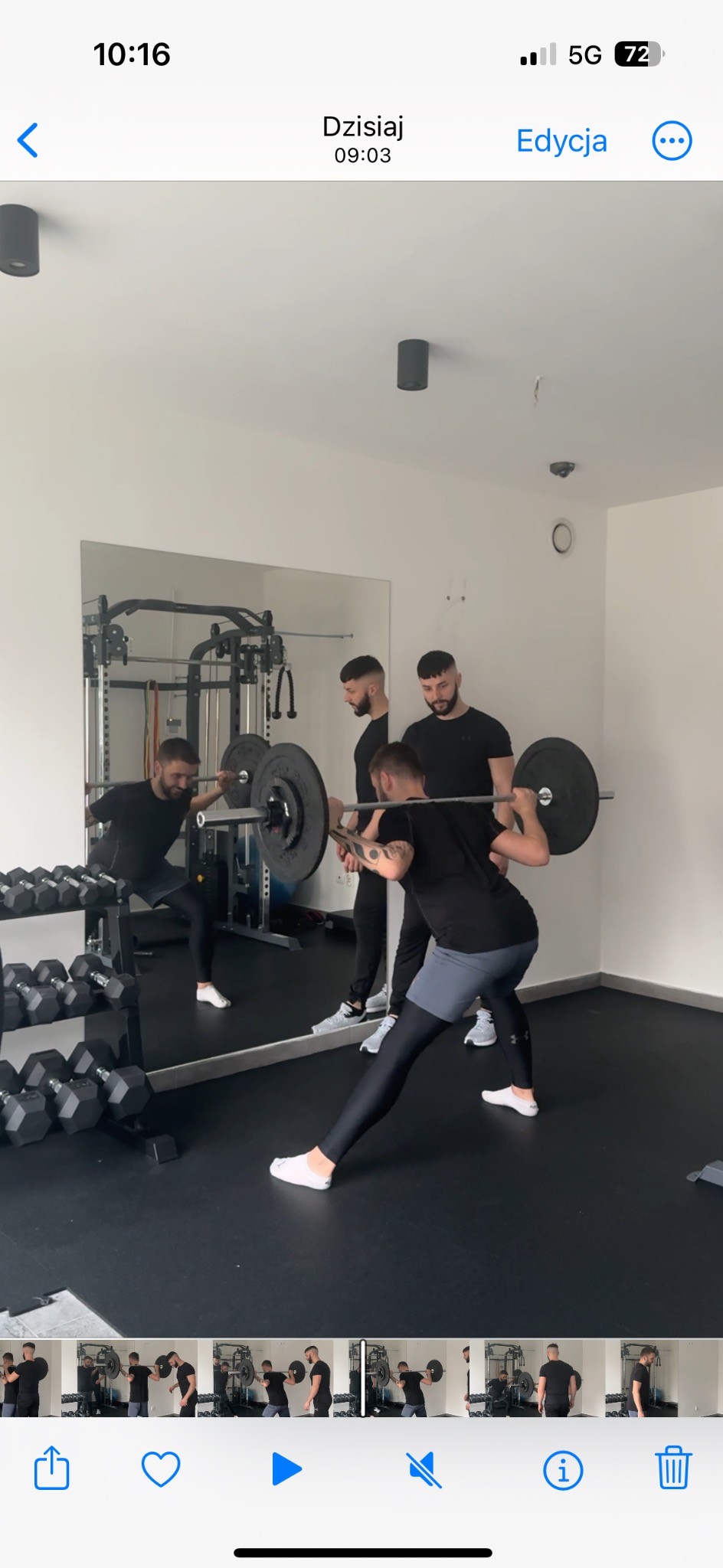 Trening siłowy z trenerem: mężczyzna wykonuje wypad z obciążeniem, asekuruje go trener. W tle lustro i stojak z hantlami. Minimalistyczne wnętrze siłowni.