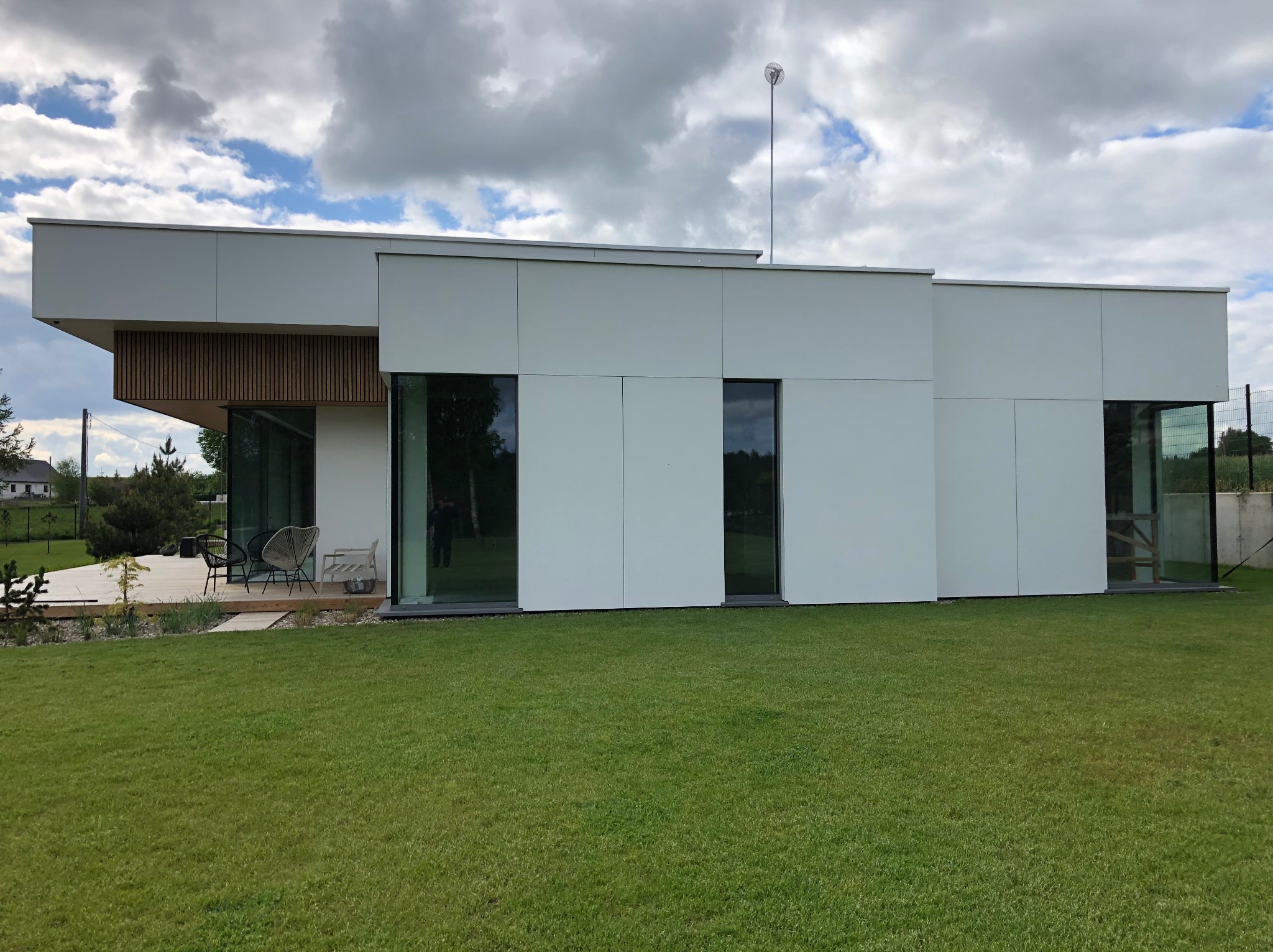 Nowoczesny dom z tarasem drewnianym i minimalistycznym ogrodem. Widoczne meble ogrodowe i starannie utrzymany trawnik.