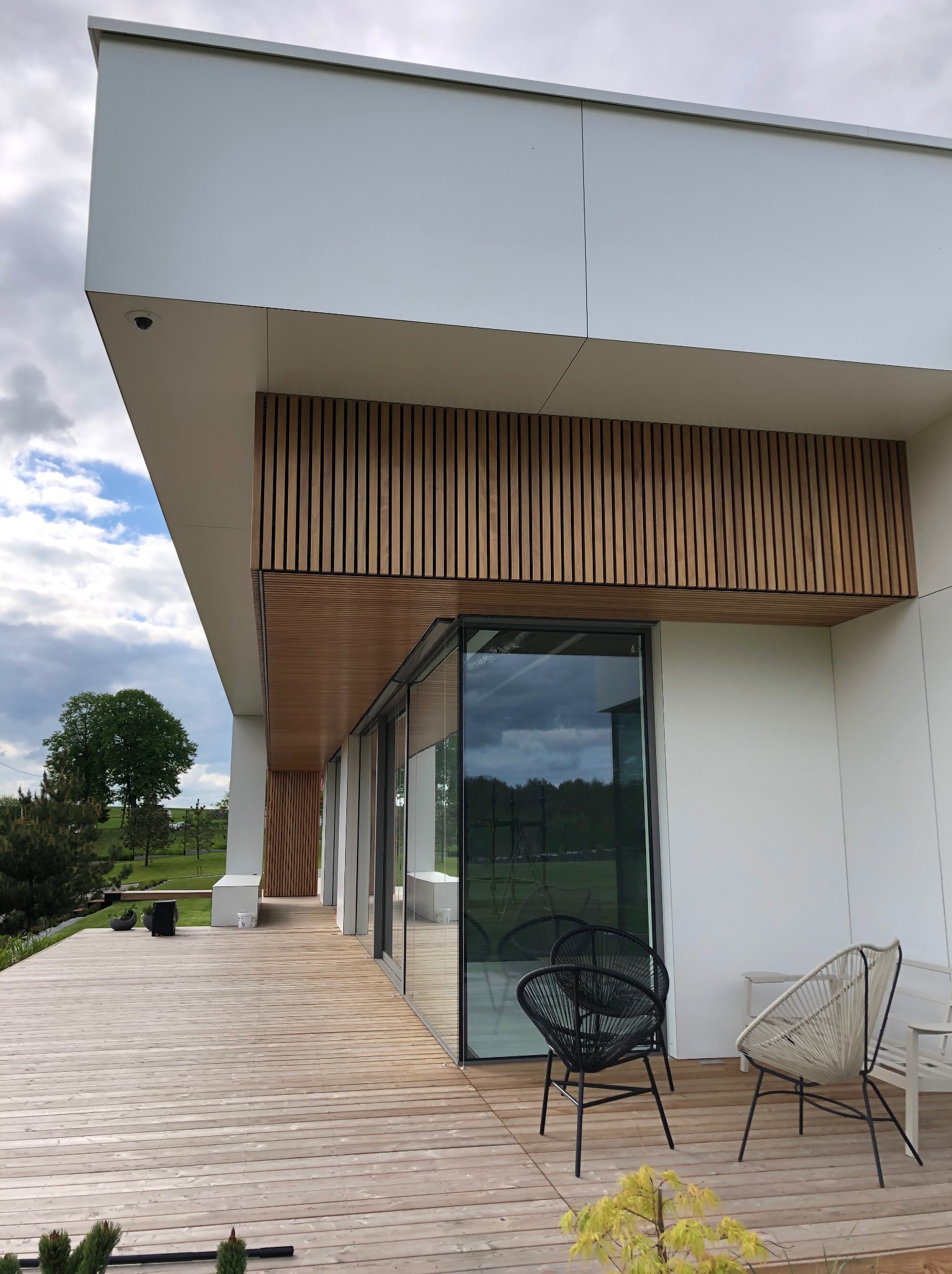 Nowoczesny taras drewniany z meblami ogrodowymi w Rokitkach. Jasne deski, minimalistyczny design, duże przesuwne okna i drewniane lamele na elewacji.
