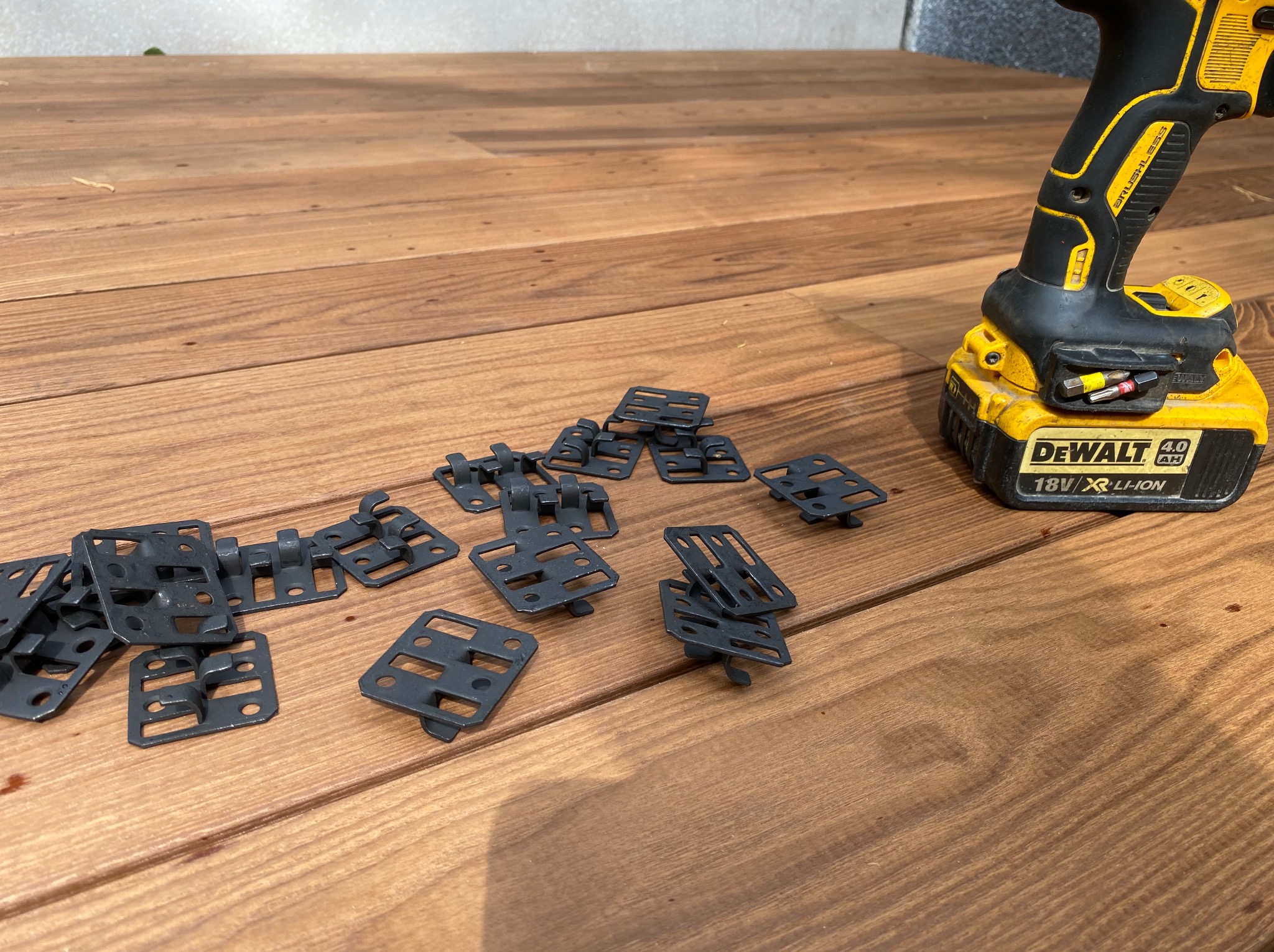 Montaż desek tarasowych: wkrętarka DeWalt i klipsy montażowe na drewnianym tarasie w ciepłym oświetleniu. Widoczne detale mocowania.