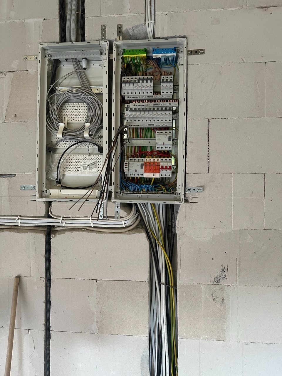 Otwarta skrzynka rozdzielcza z okablowaniem na surowej ścianie z betonu komórkowego. Widoczne liczne przewody i zabezpieczenia. Etap prac instalacyjnych.