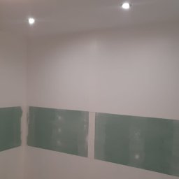 Usługi budowlane - Ściana z zamontowanymi płytami kartonowo-gipsowymi, przygotowana do dalszych prac wykończeniowych. Widoczne punkty oświetleniowe w suficie.