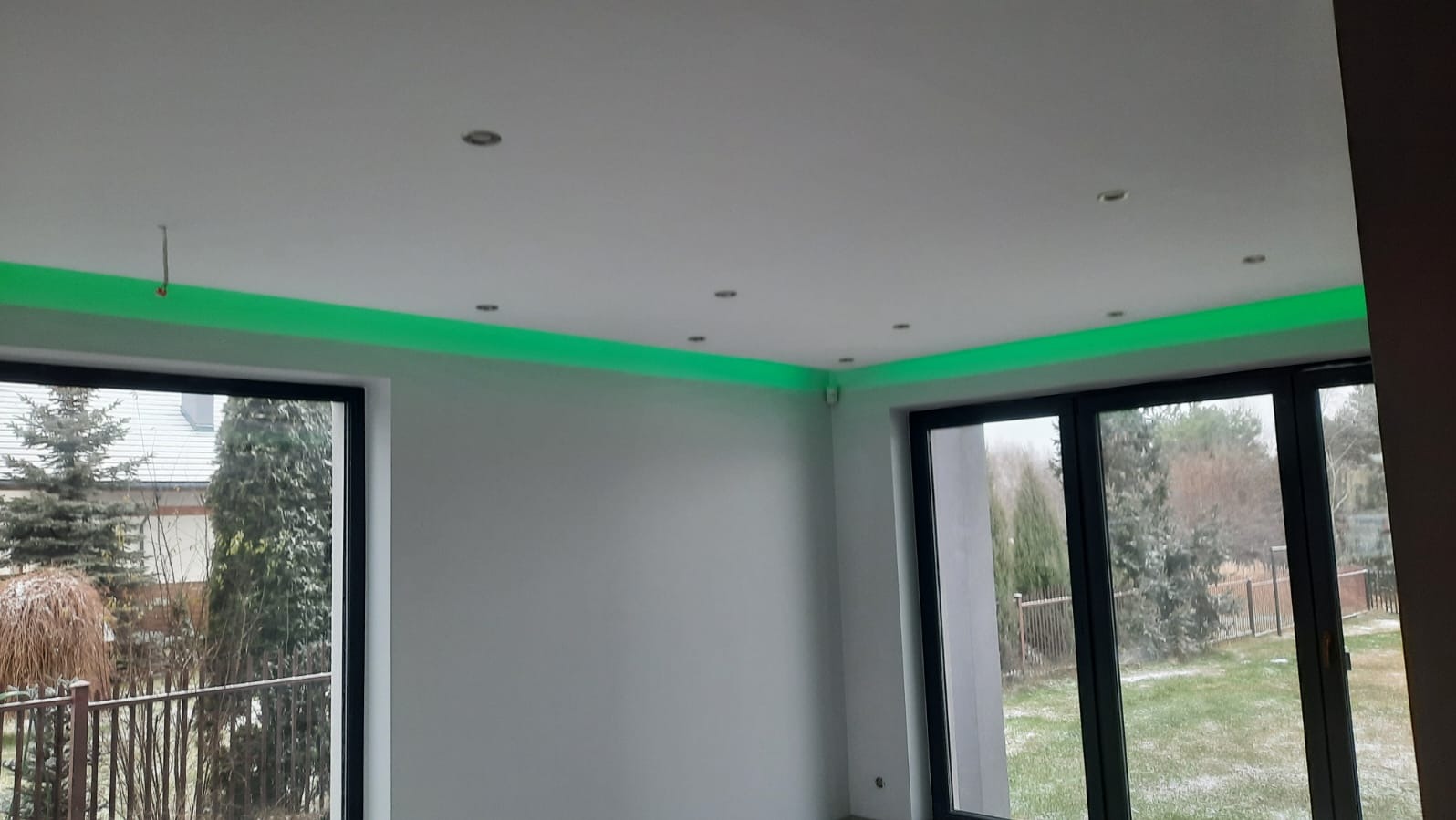 Nowoczesne wnętrze z oświetleniem LED w kolorze zielonym, umieszczonym pod sufitem. Widoczne okna z widokiem na zewnątrz i punktowe oświetlenie sufitowe.