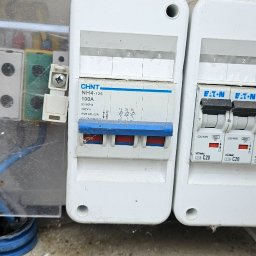 Piotr Meller Energia w Dobrym Klimacie - Rozdzielnica elektryczna z bezpiecznikami CHNT i EATON, widoczne przewody i elementy montażowe. Instalacja w skrzynce z przezroczystą osłoną.