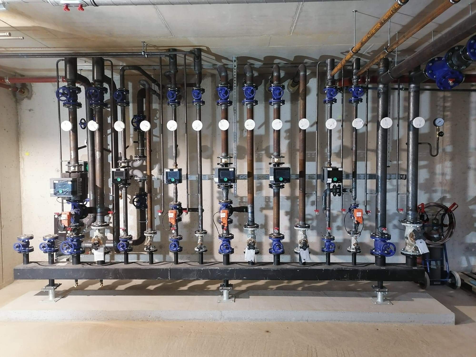 Złożona instalacja hydrauliczna z rurami, zaworami i miernikami w pomieszczeniu technicznym. Widoczne elementy montażowe i podłączenia.