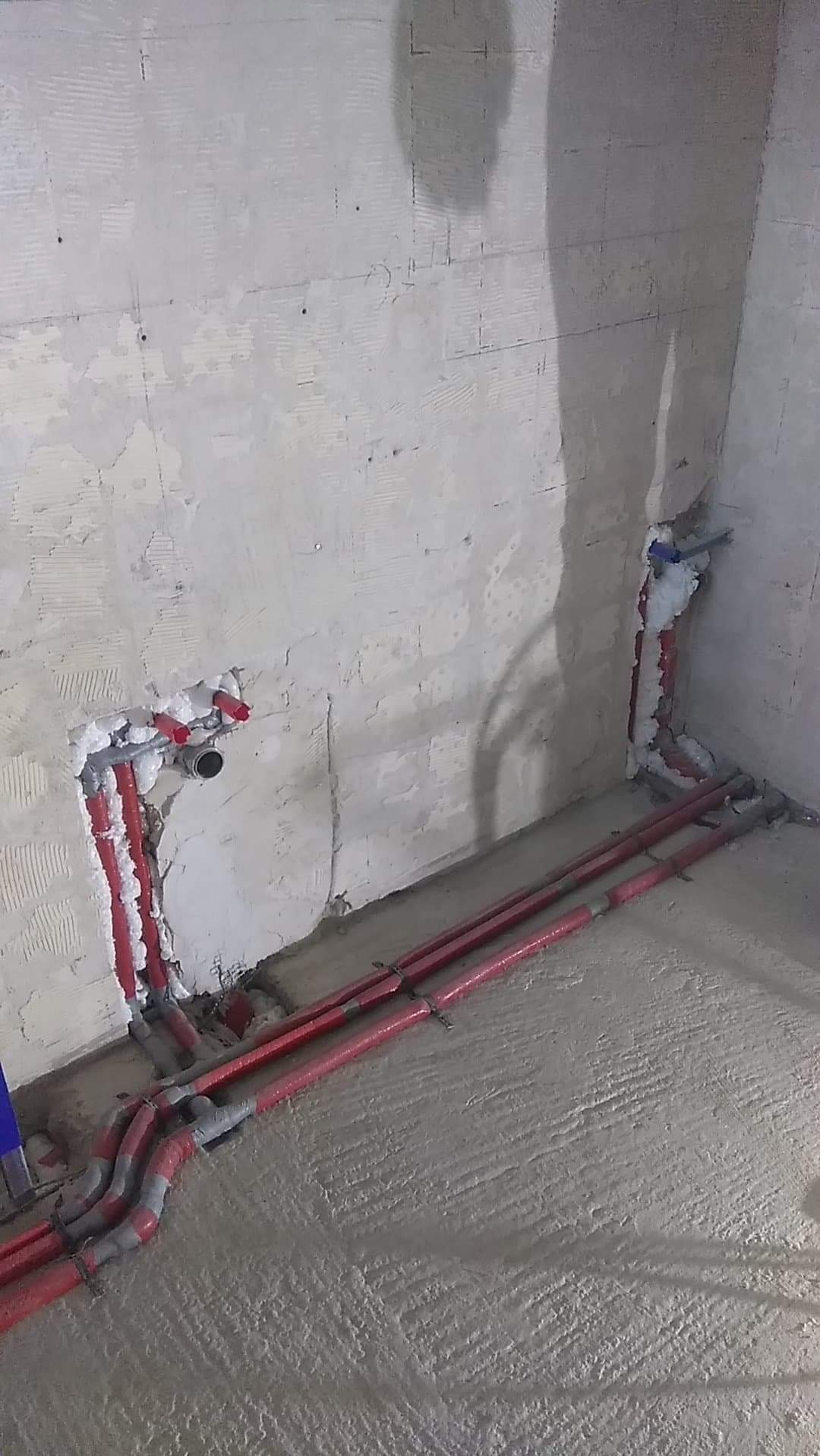 Czerwone rury instalacji hydraulicznej, zabezpieczone pianką montażową, prowadzone wzdłuż surowej ściany i podłogi w trakcie prac wykończeniowych.
