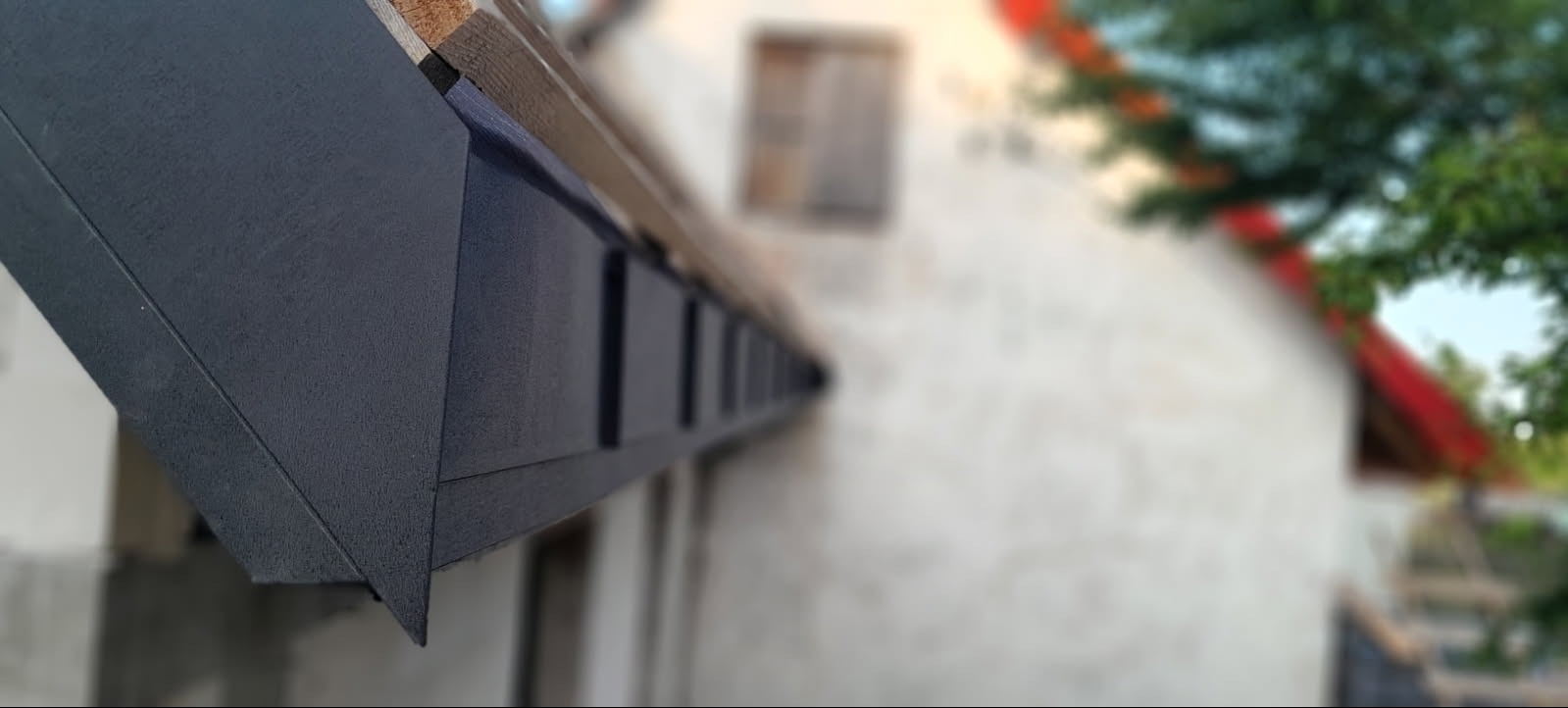 Szczegółowe ujęcie nowej, grafitowej podbitki dachowej z widocznymi elementami konstrukcji drewnianej na tle budynku z czerwoną dachówką.