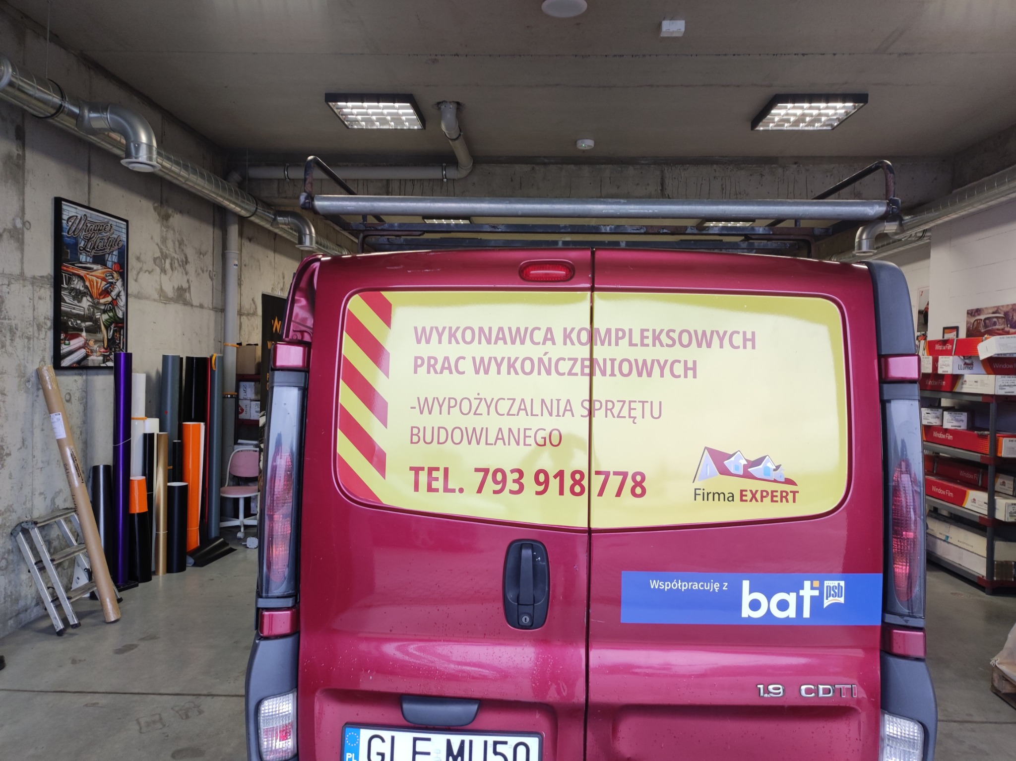 Tył czerwonego busa z reklamą firmy EXPERT, oferującej kompleksowe prace wykończeniowe i wypożyczalnię sprzętu budowlanego. Widoczne numery telefonu i logo firmy.