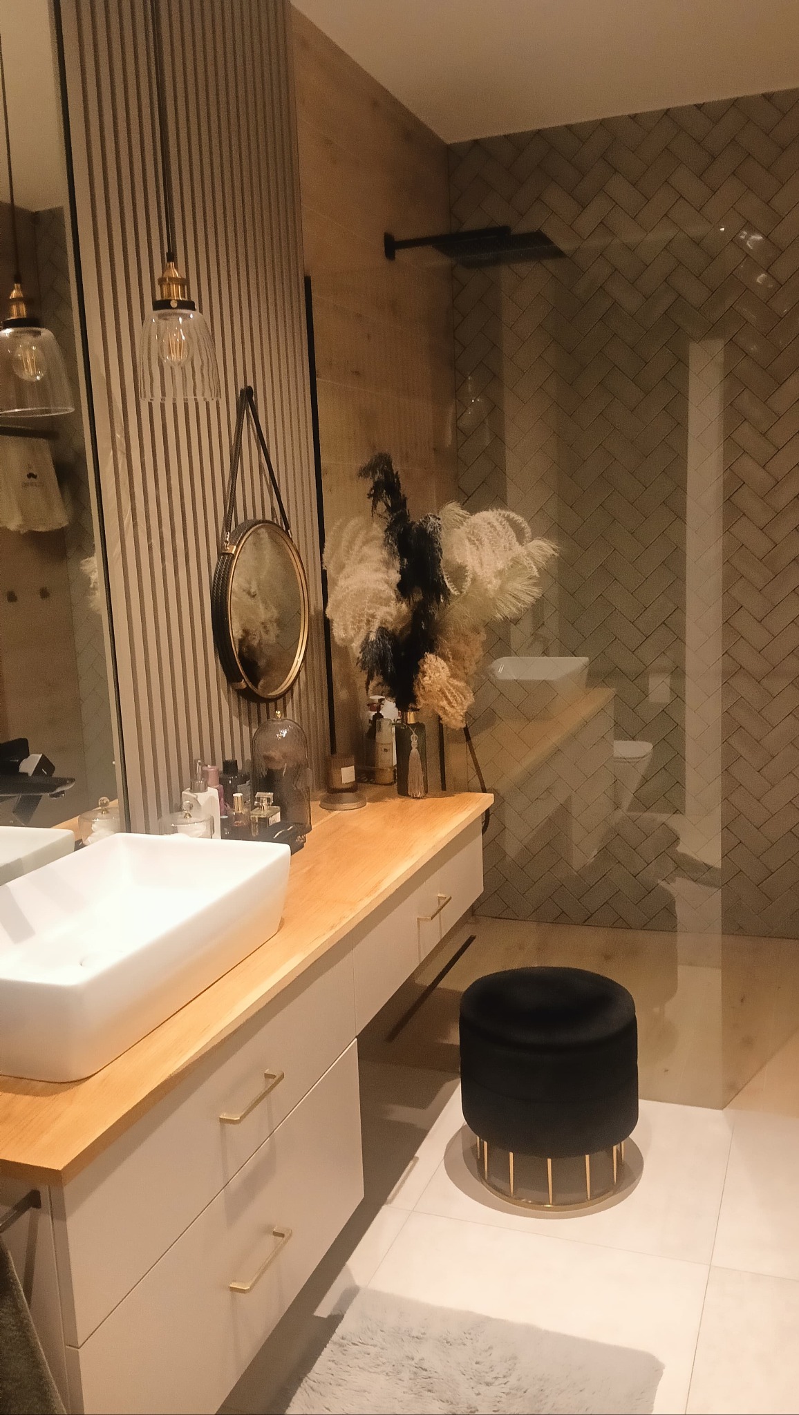 Nowoczesna łazienka w Tykocinie z umywalką nablatową, drewnianymi akcentami i kabiną prysznicową wyłożoną płytkami w jodełkę. Stylowe oświetlenie i dekoracje.