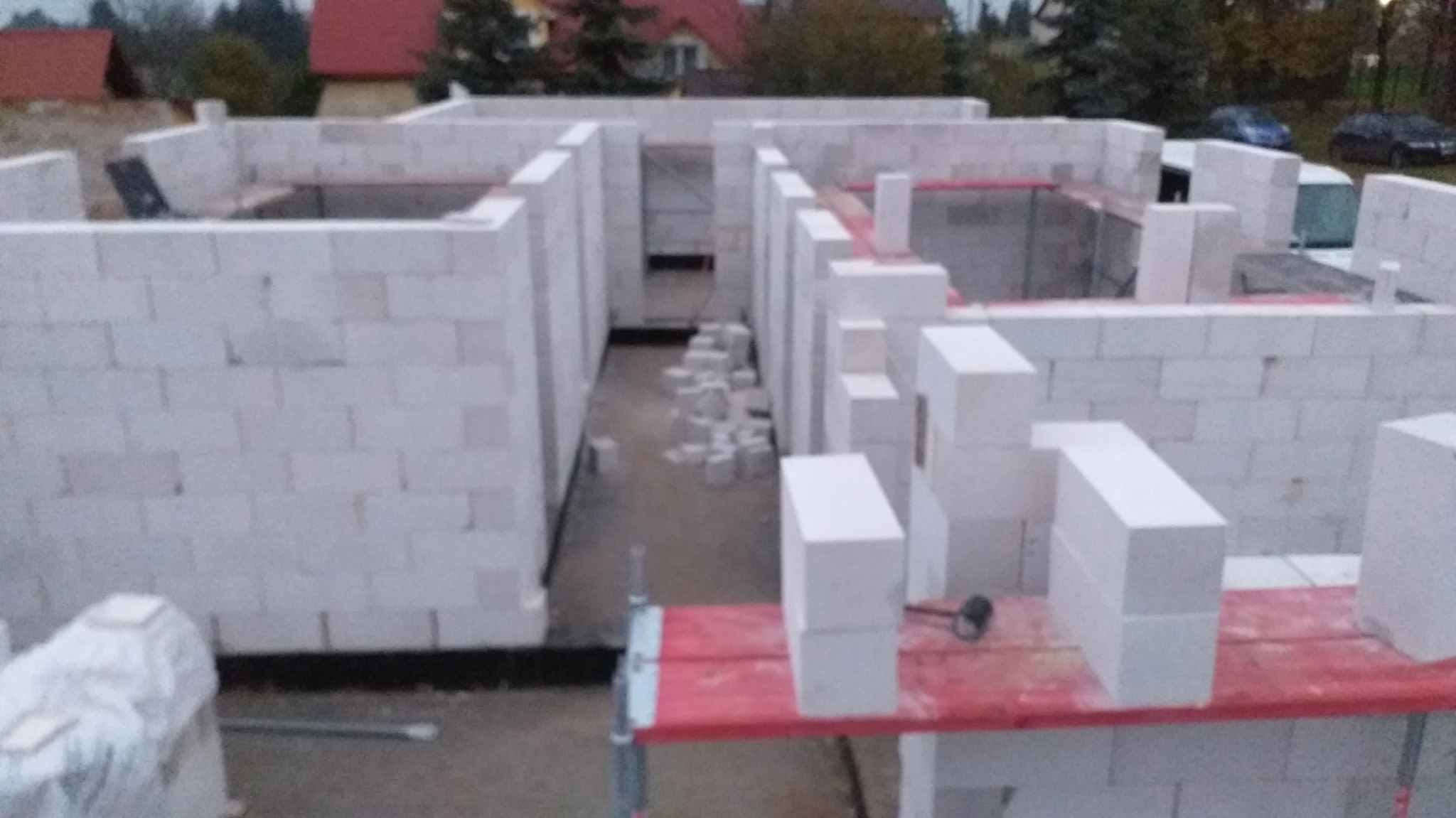 Wznoszenie ścian działowych z białych bloczków betonu komórkowego. Widoczne fragmenty rusztowania i narzędzia murarskie. Budowa domu w trakcie realizacji.