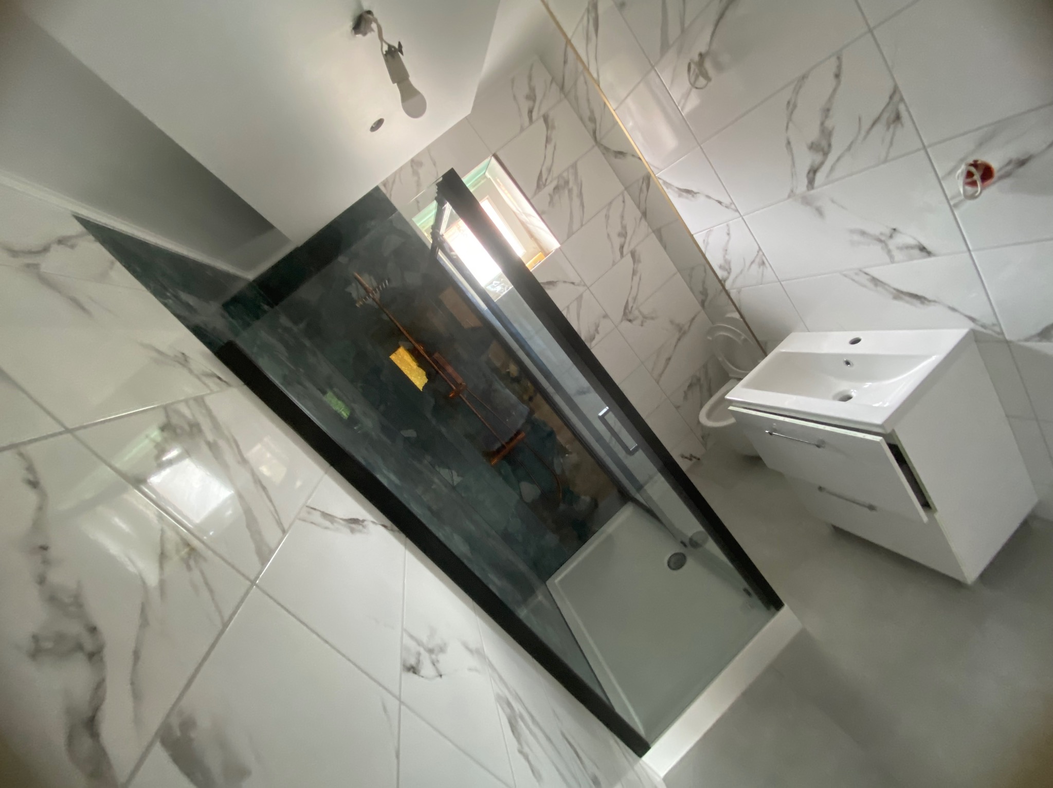 Nowoczesna łazienka z kabiną prysznicową typu walk-in, białą umywalką z szafką i marmurowymi płytkami. Widok z dołu, podkreślający przestronność i minimalistyczny design.